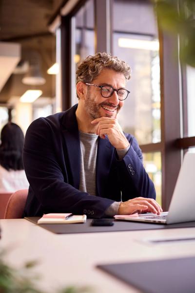 Mature Businessman Wearing Glasses Working On Laptop At Desk In Office
