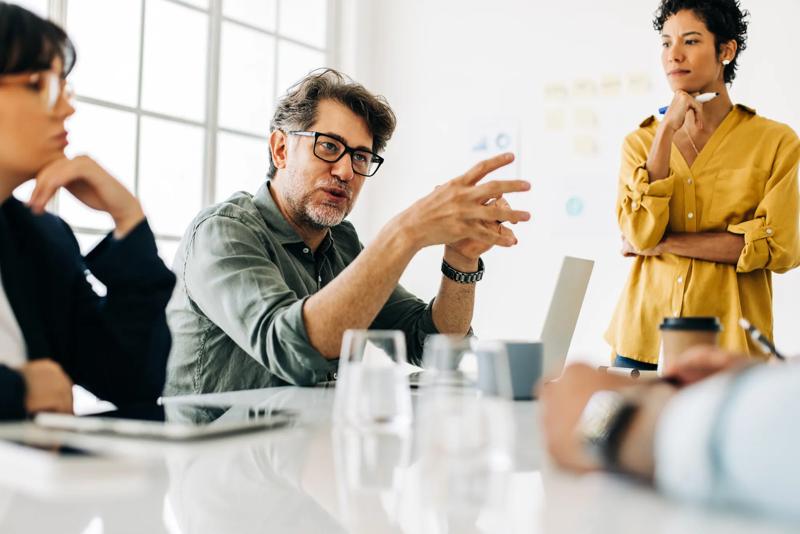 Business man explaining a project to his team. Senior business man taking the lead during a meeting. Group of business people discuss about work in an office.