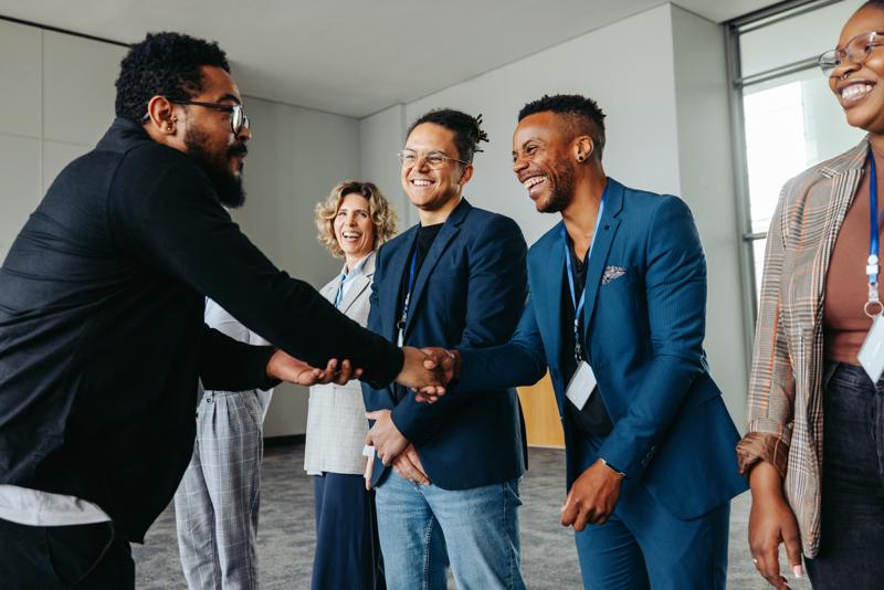Diverse group of professionals greeting each other with handshakes at a corporate conference event in an office setting.