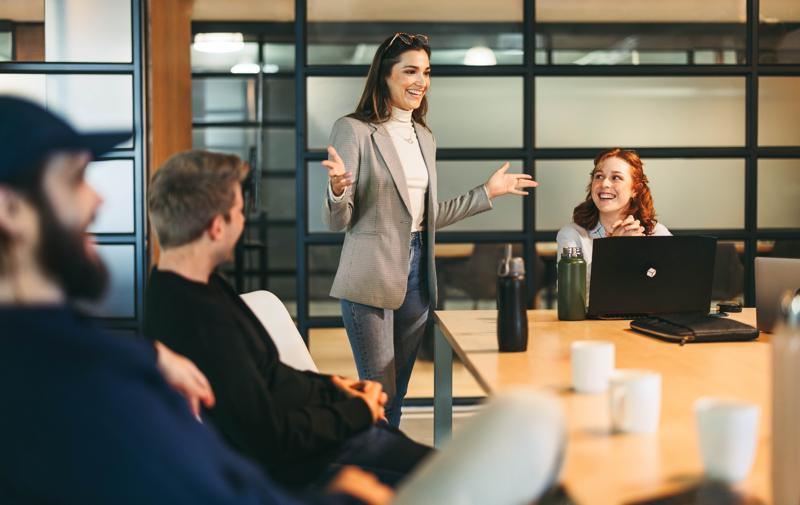 Diverse professionals, both men and women, brainstorming and discussing ideas in a lively office meeting. Led by a charismatic leader, this successful tech startup exemplifies the power of teamwork in project management.