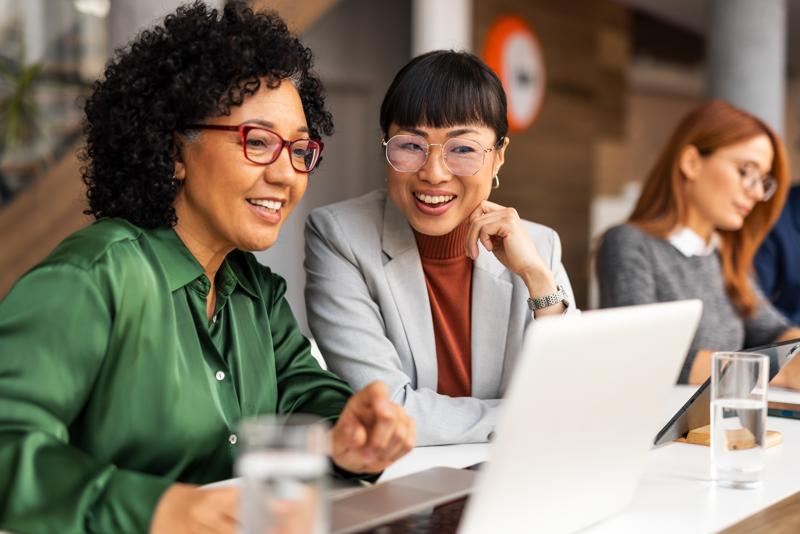 Professionals working together in a collaborative office environment, engaging in positive discussions with laptops, exhibiting teamwork and productivity. Office setting fosters innovation and mutual respect.