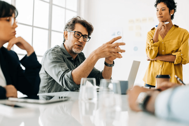 Business man explaining a project to his team. Senior business man taking the lead during a meeting. Group of business people discuss about work in an office.