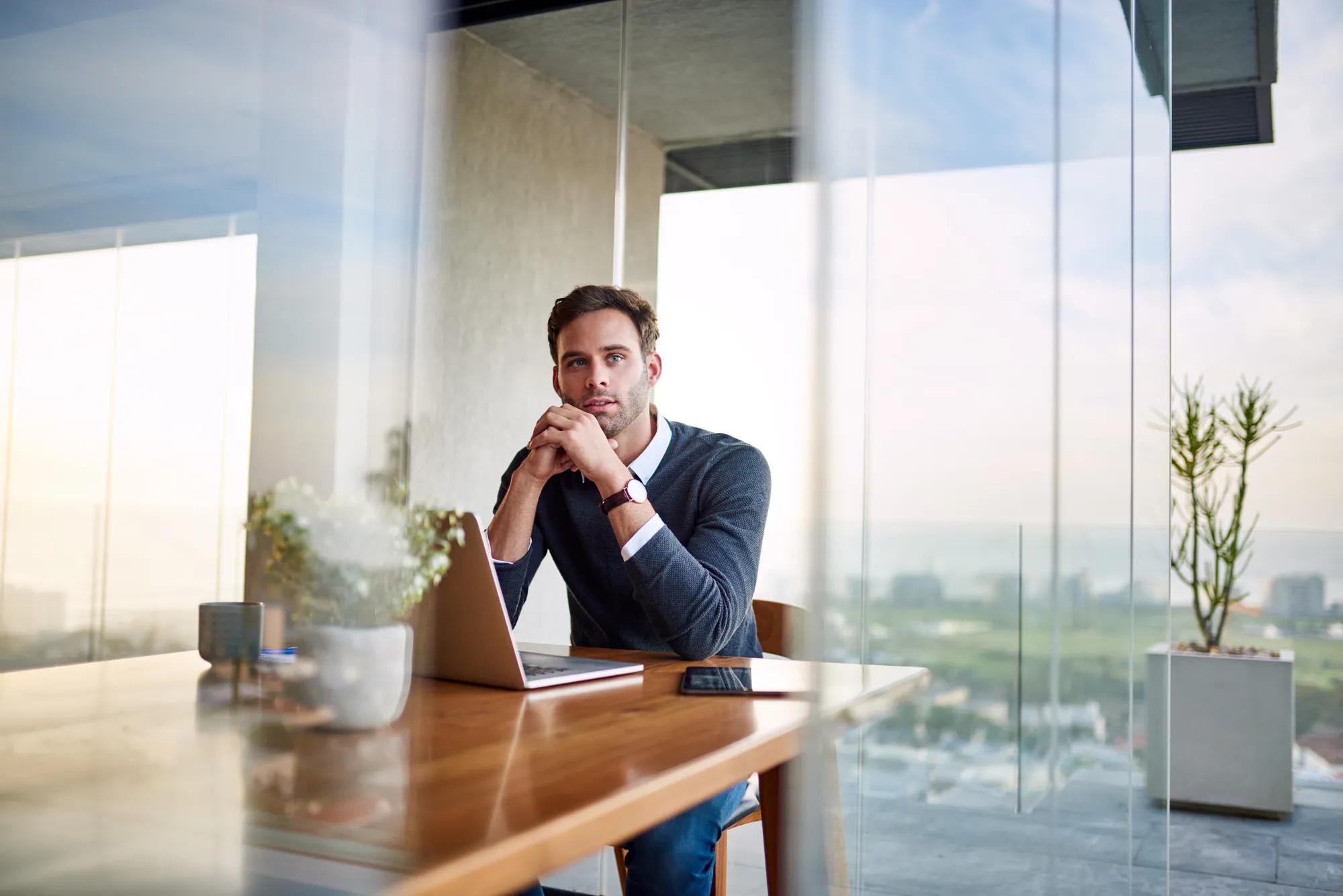 Young businessman deep in thought while sitting at a table at home and working on a laptop
