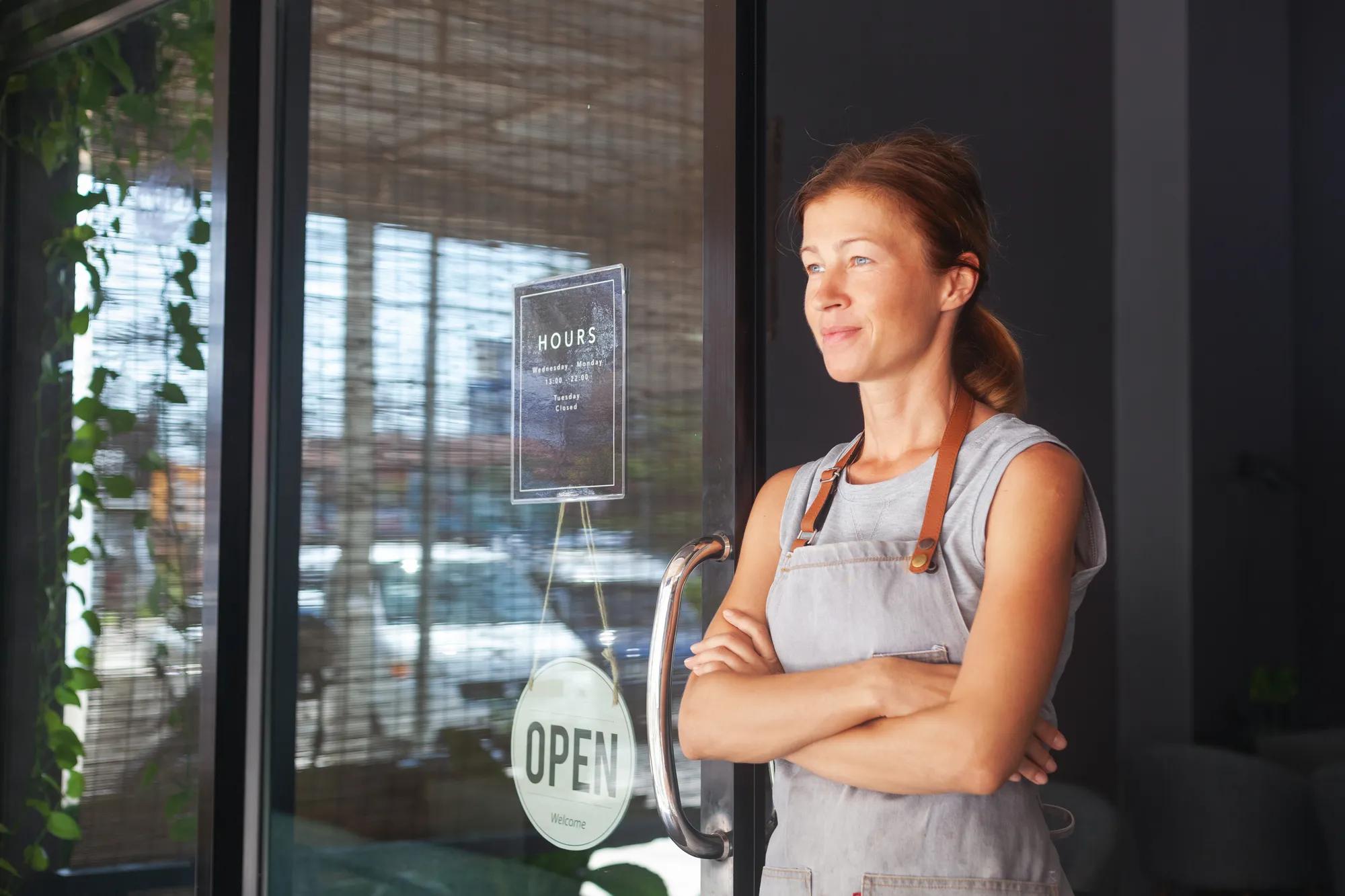 A female waitress, the owner of a cafe sits in the door of a cafe with a sign Open waiting for customers. Small business concept, cafes and restaurants