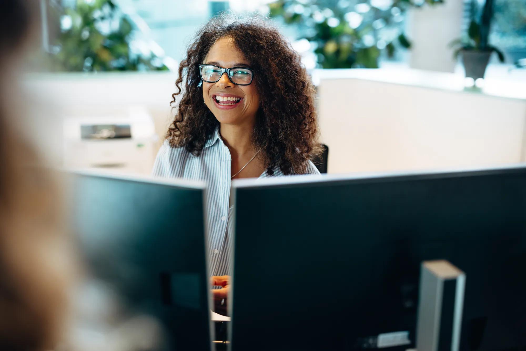 Smiling woman working at front desk of a municipality office. Female administrator sitting behind the desk looking at a woman and smiling.