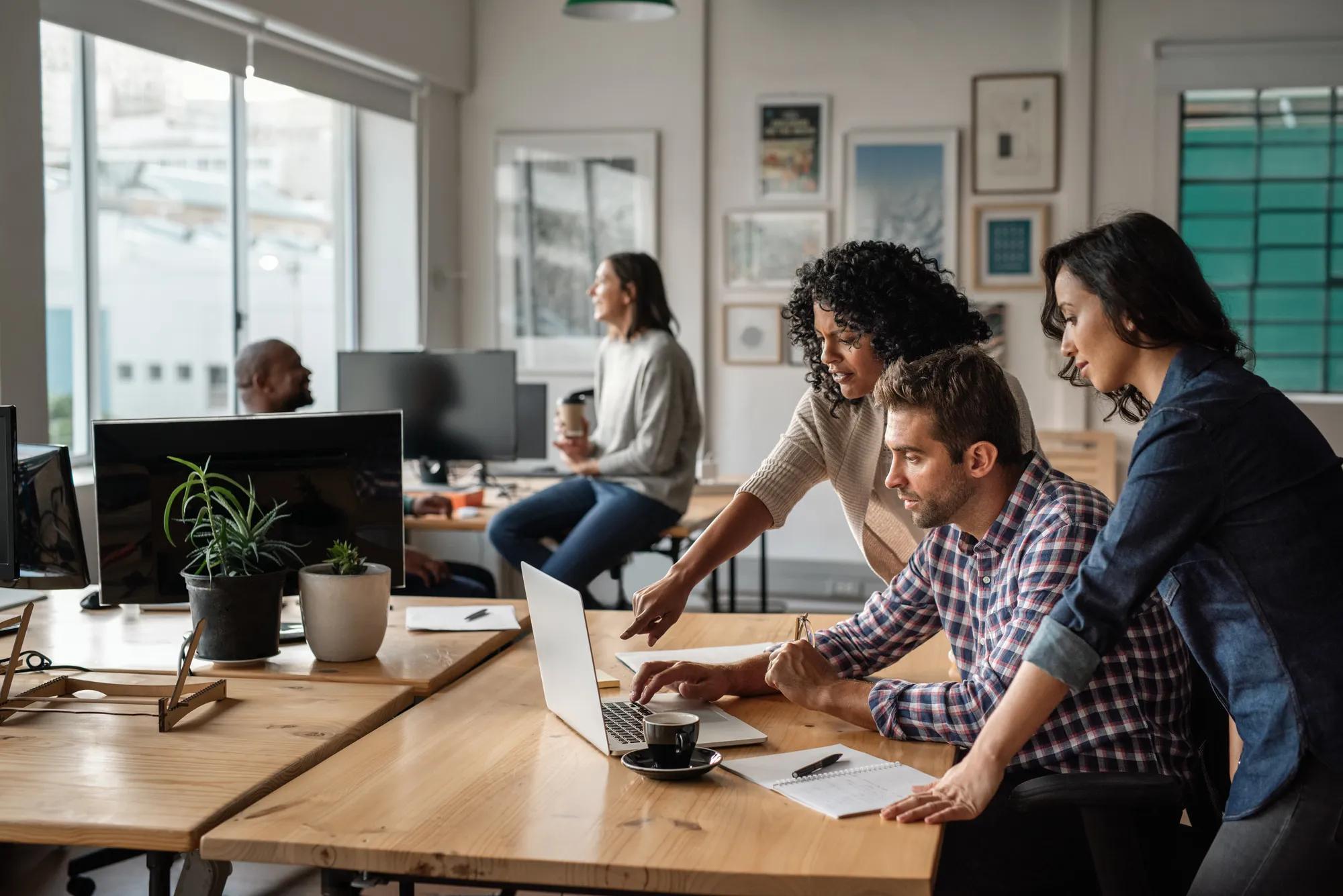 Focused group of diverse young designers working on a laptop together at a desk in their startup office