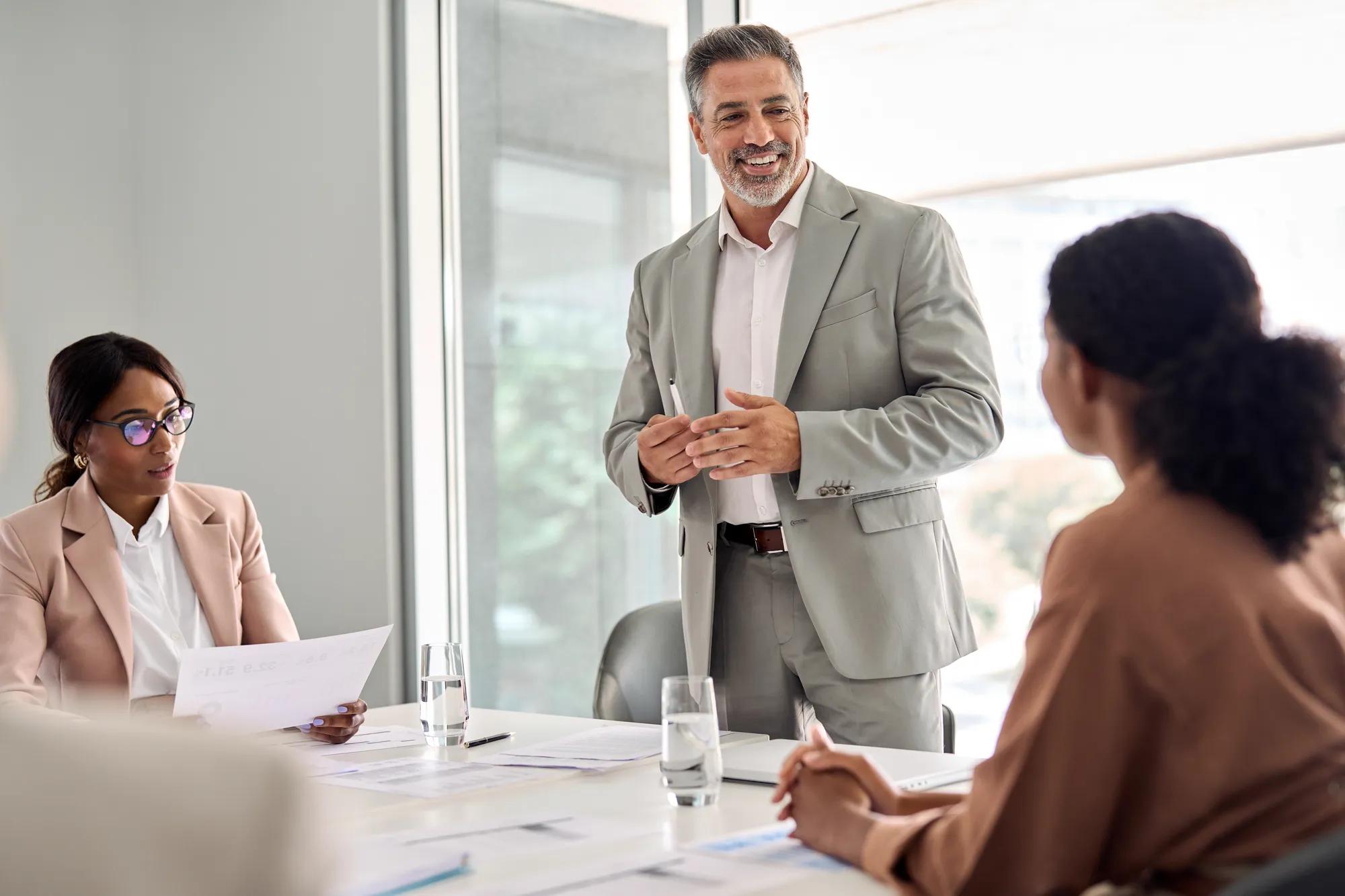 Busy older manager leader and company employees at business meeting discussing corporate management. International professional business people board team at boardroom office table.