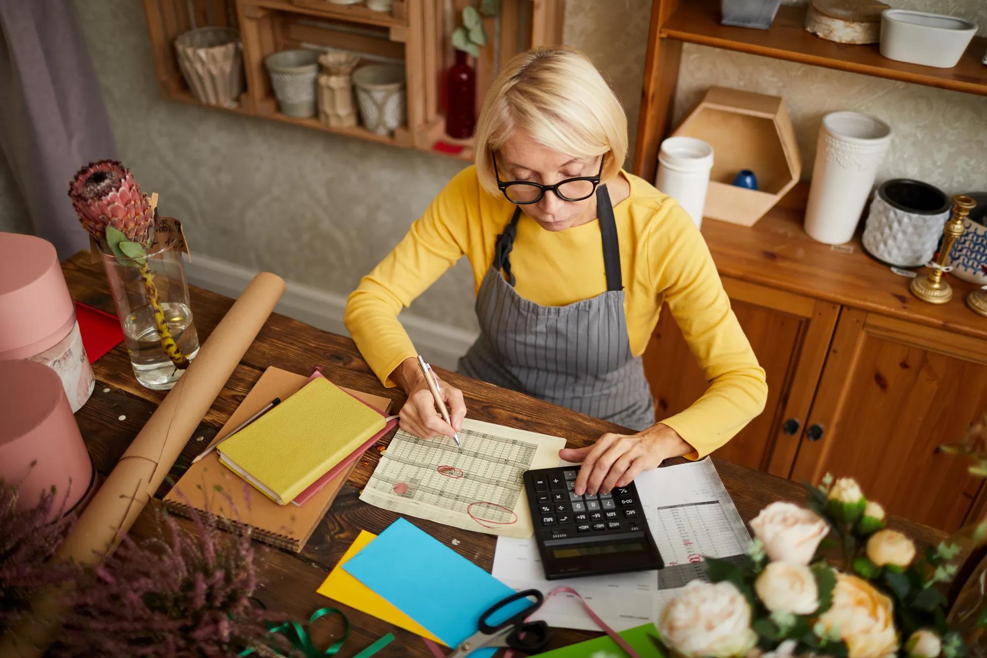 High angle portrait of female businesswoman counting finances using calculator in small shop, copy space