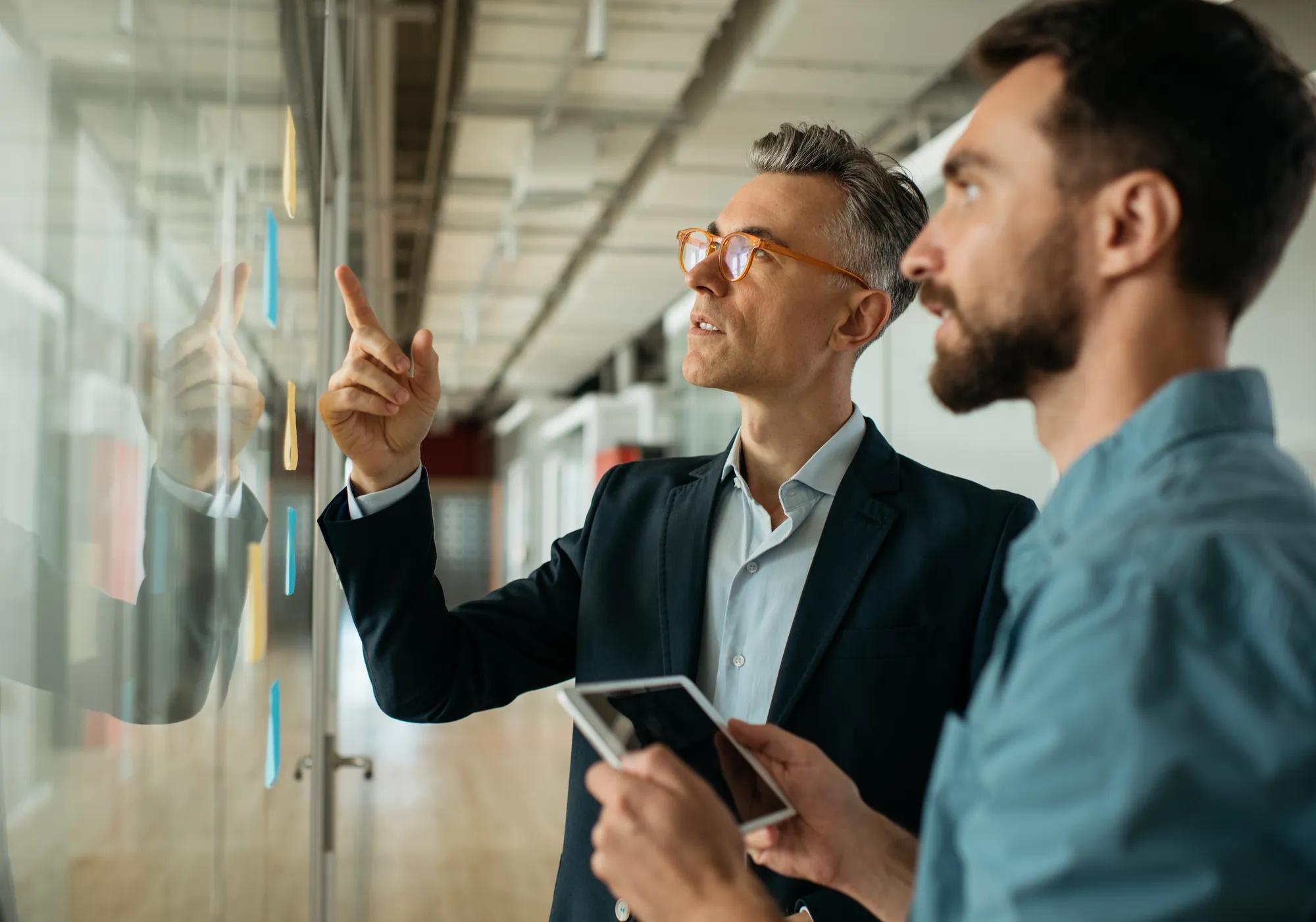 Two business men discussing in modern office with sticky notes.