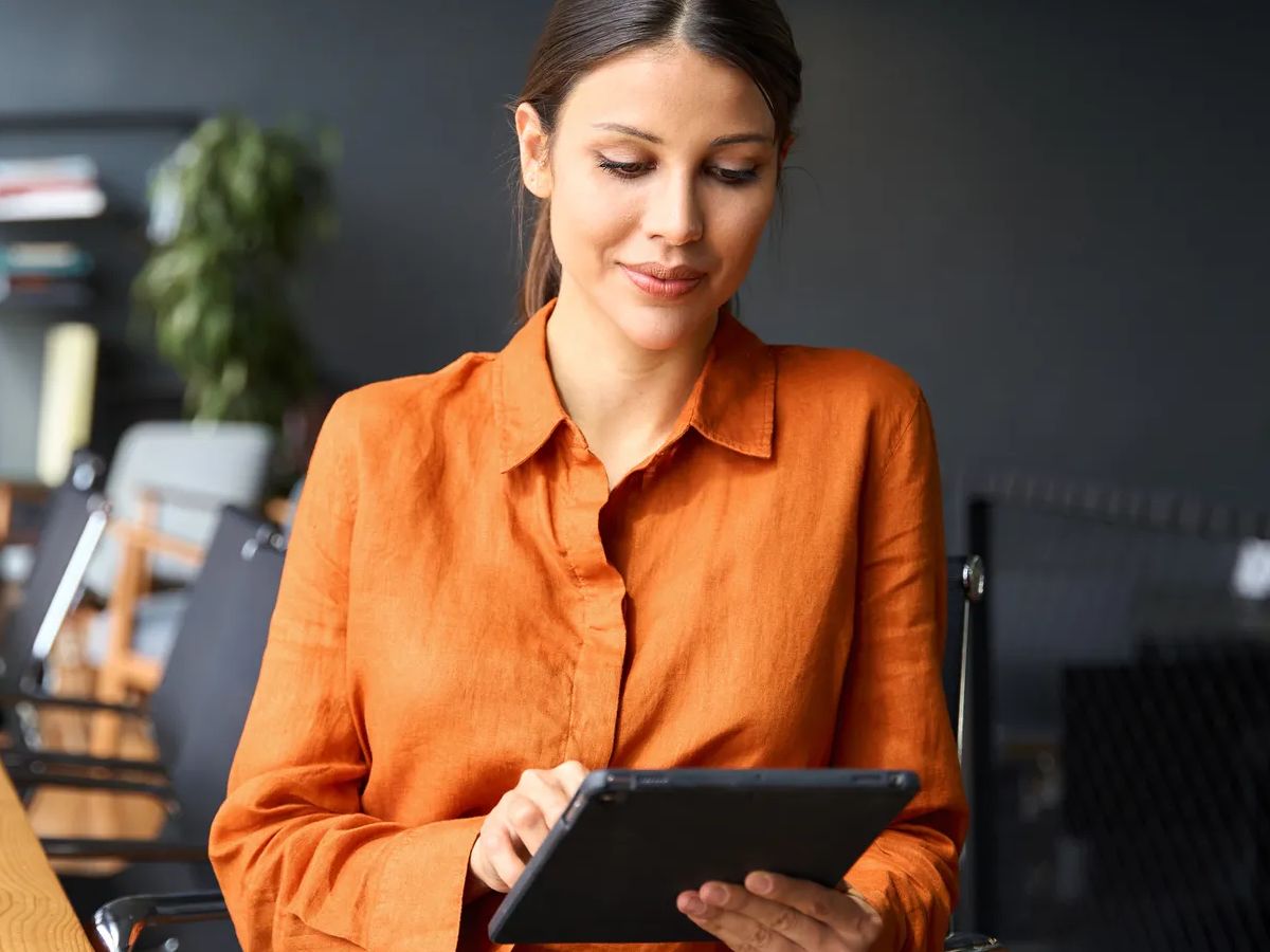 Successful smiling latin hispanic young woman using pad computer for business app. Busy executive CEO businesswoman professional holding digital tablet pc device for work in modern office workplace. 