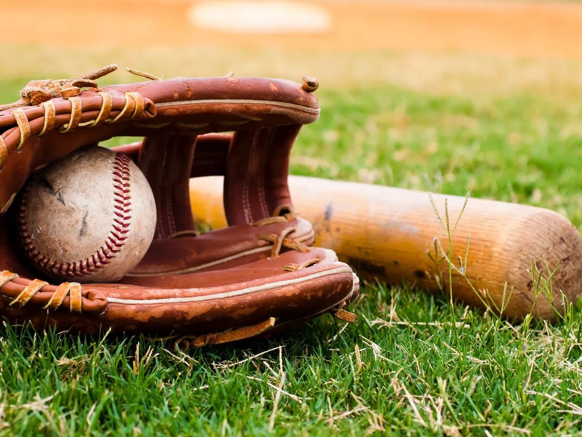 Old baseball, glove, and bat on field with base and outfield in background.