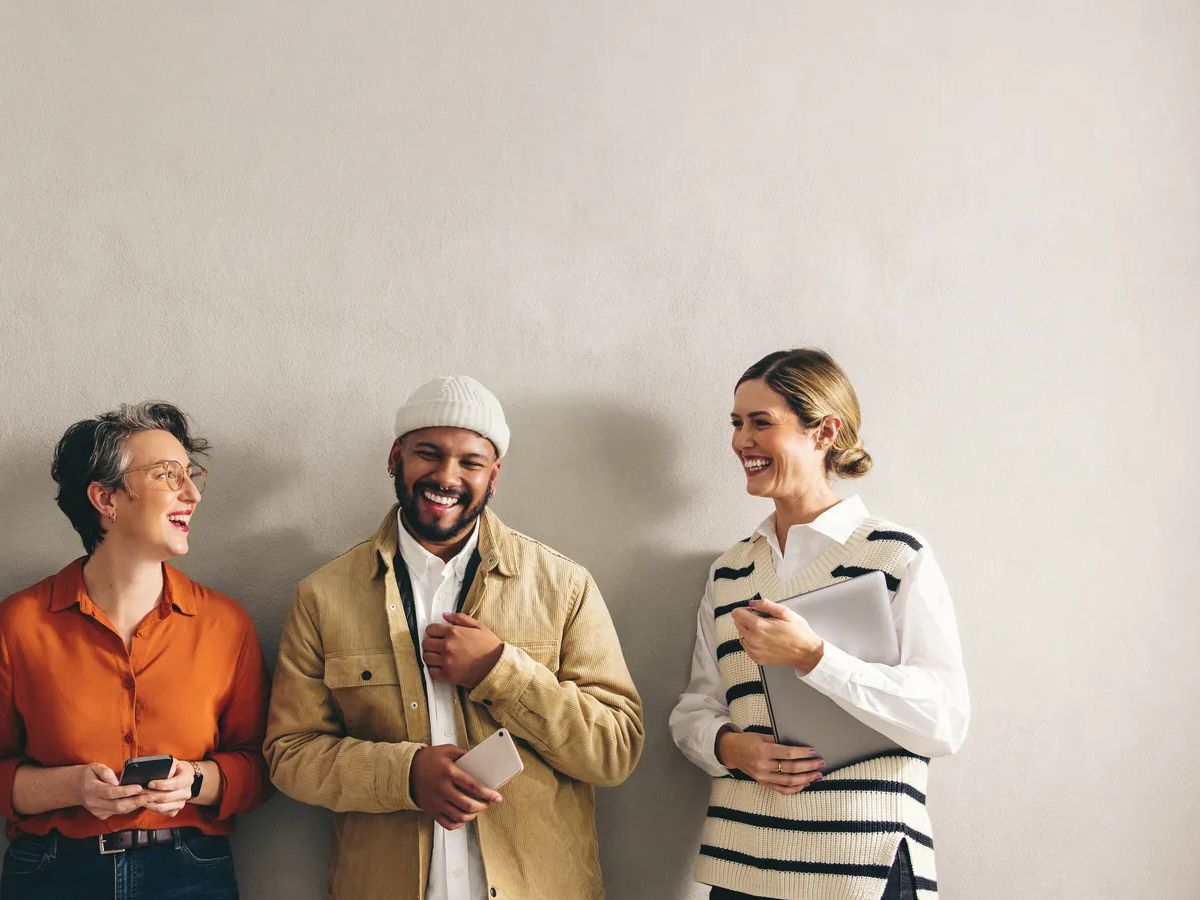 Happy businesspeople smiling cheerfully while waiting in line for an interview. Group of shortlisted job candidates holding different digital devices in a modern workplace.