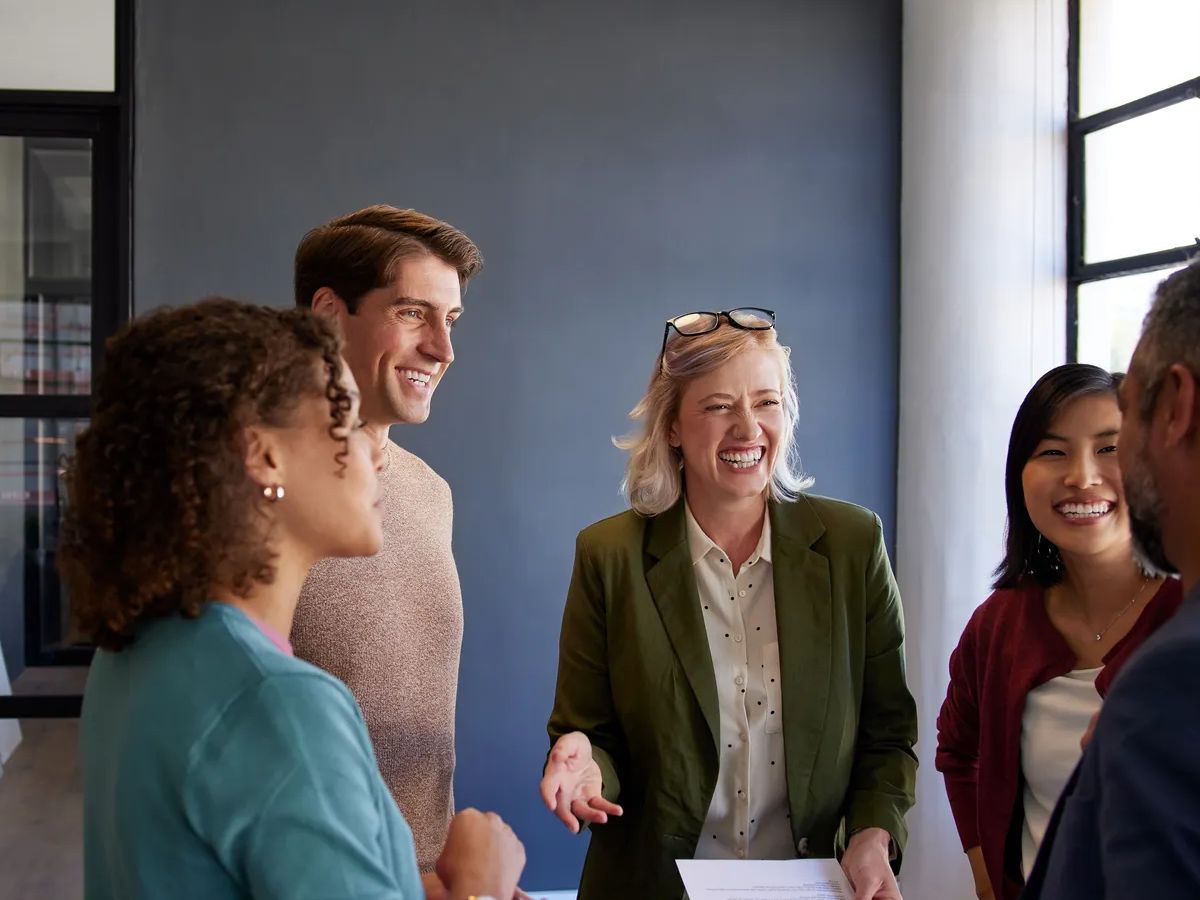 Group of multiethnic professionals sharing conversation in office. Happy business team laughing and engaging in a casual discussion. Group of casual business people in a casual metting talking on business report with copy space.