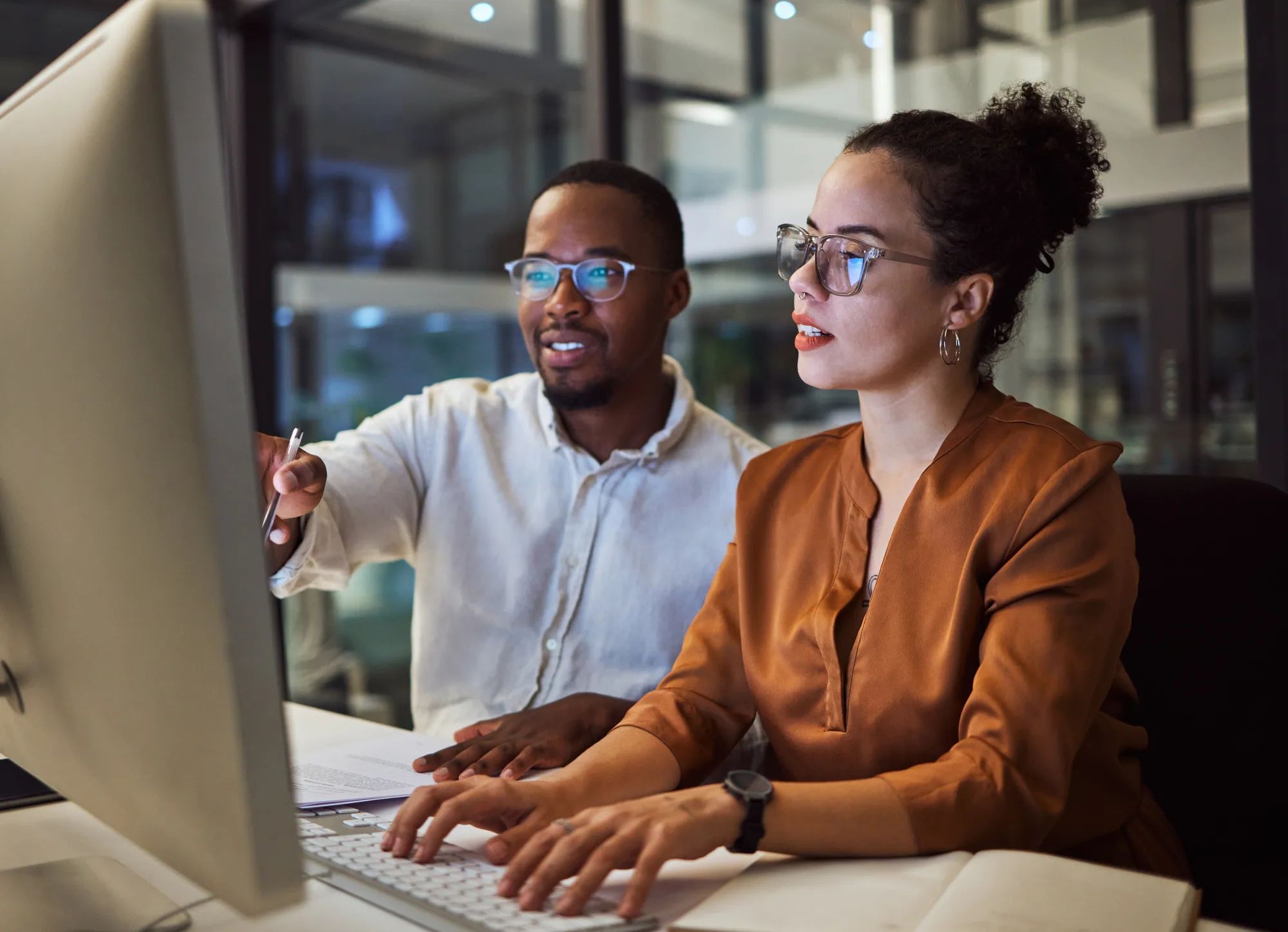 Night training, teamwork and employees planning marketing strategy in a dark office on computer at work. Corporate African man and woman talking about business collaboration during overtime together.
