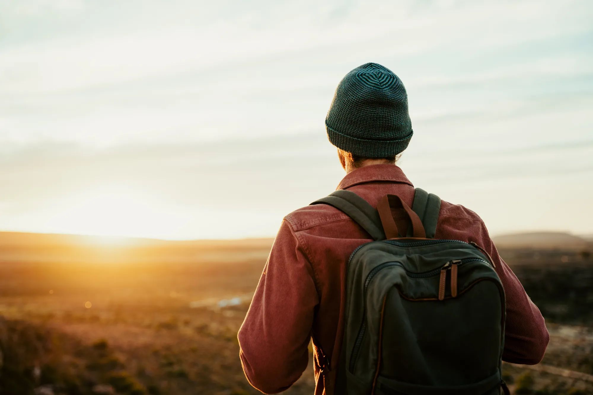 Caucasian male free spirit wearing beanie walking through wilderness watching sunset over horizon . High quality photo