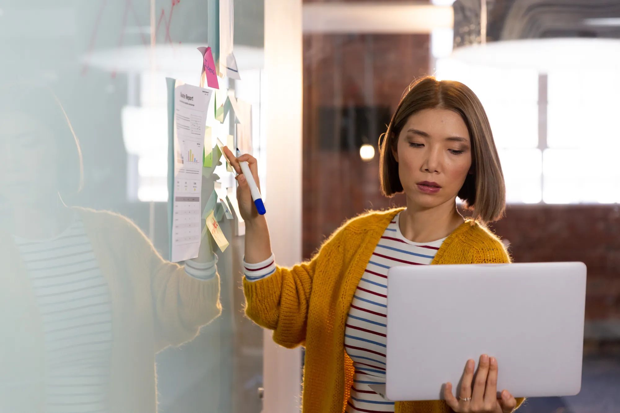 Asian businesswoman standing in front of whiteboard and writing holding laptop having video call