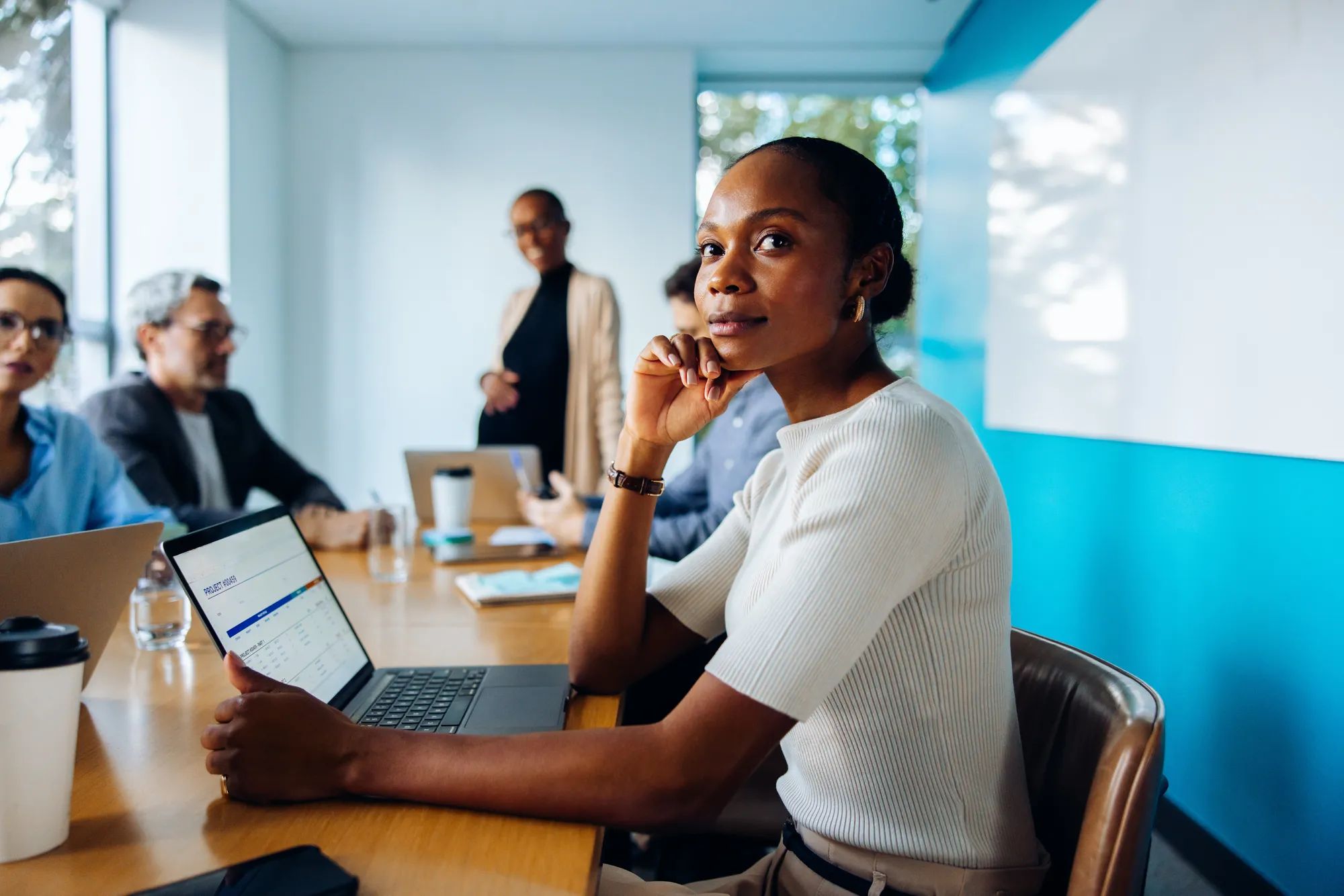 A diverse group of professionals having a meeting in a bright office space. The scene highlights a confident and thoughtful woman as the focus.
