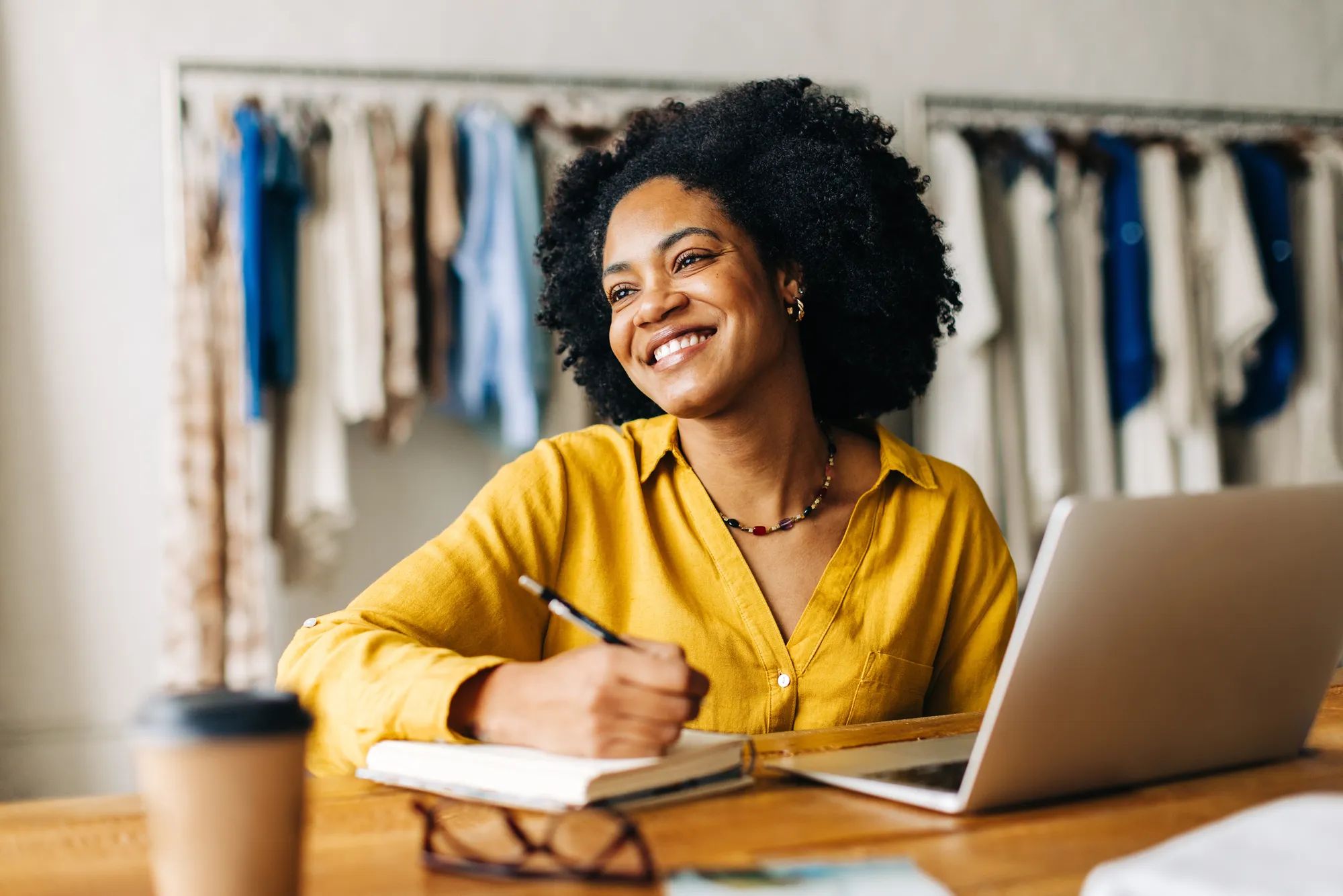 Happy fashion designer smiling confidently as she writes down plans for her small business in a note book. Creative young woman using her entrepreneurial ideas in running a clothing store.