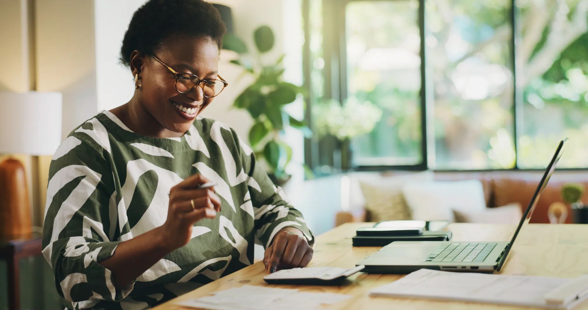 Happy, black woman and finance with laptop for payroll, tax return or budget planning at home. Female person, accounting or smile with calculator, documents or bills for expenses, deductions or audit.