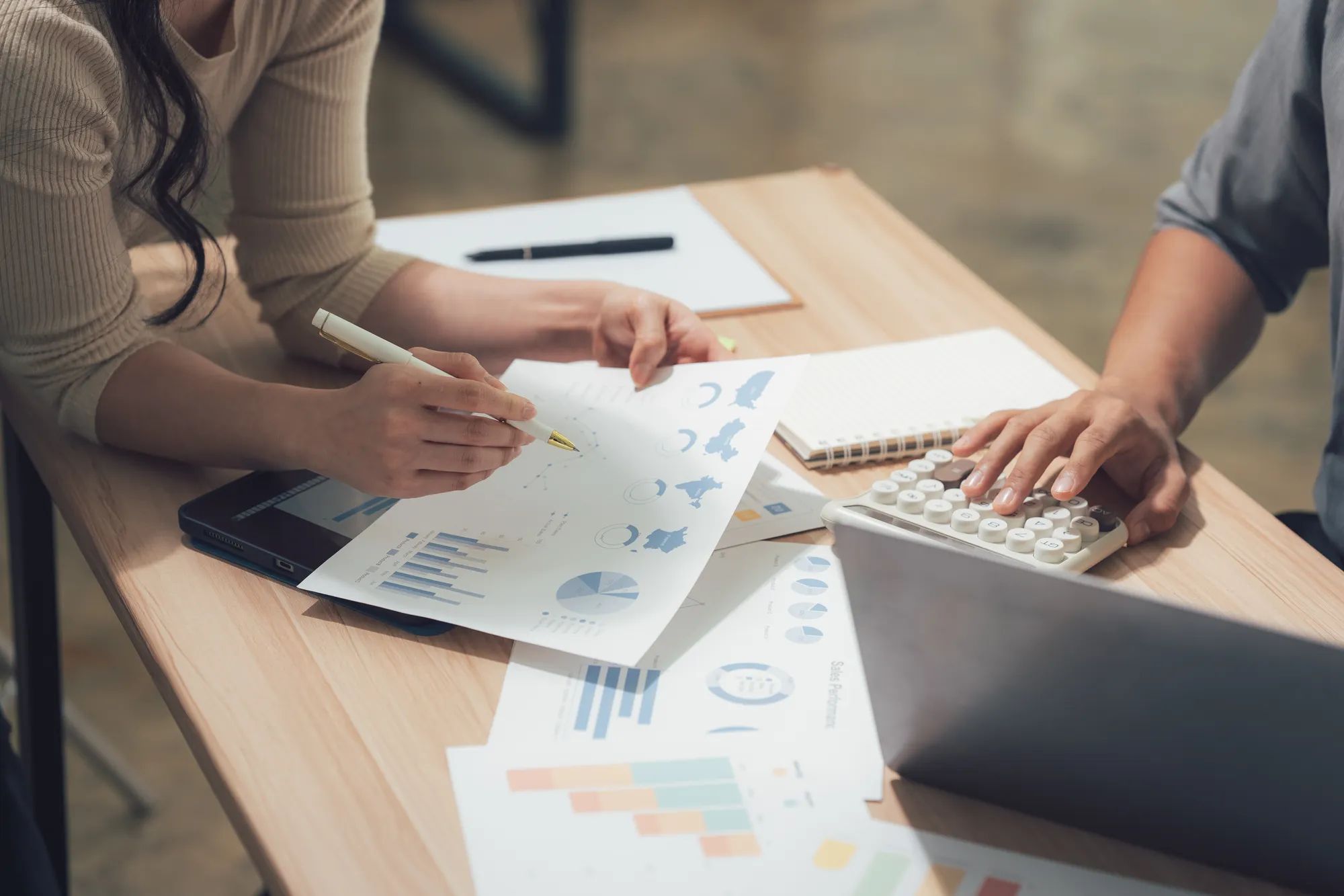 Collaboration and Analysis: Two individuals work together, meticulously reviewing data and utilizing a calculator, indicating a detailed financial analysis in a modern workplace setting.