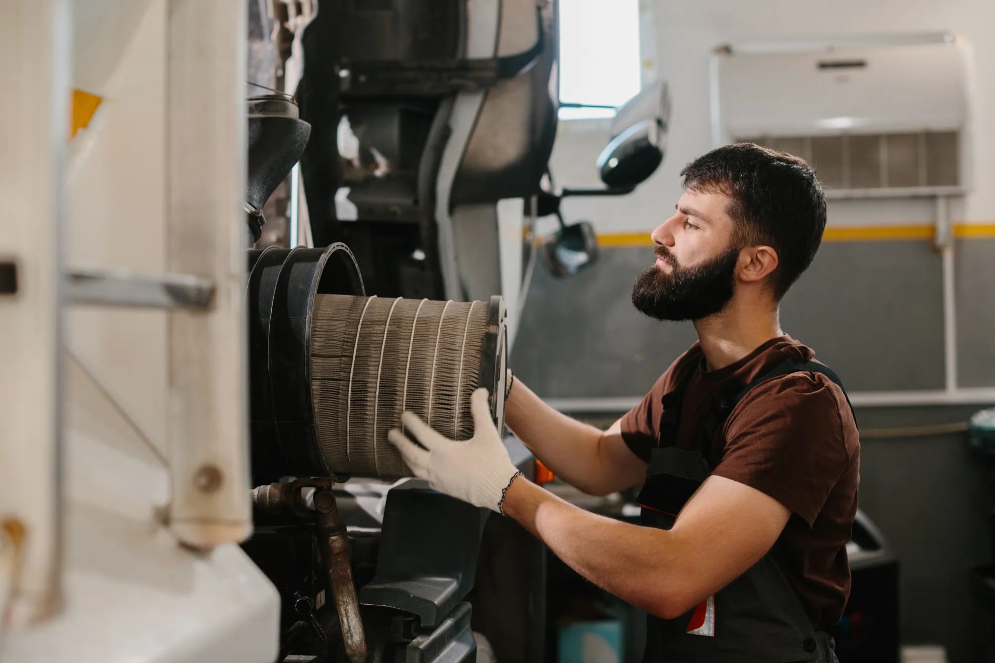 Mechanic wearing gloves is changing a dirty air filter in a truck at a busy repair shop, ensuring optimal engine performance and maintenance
