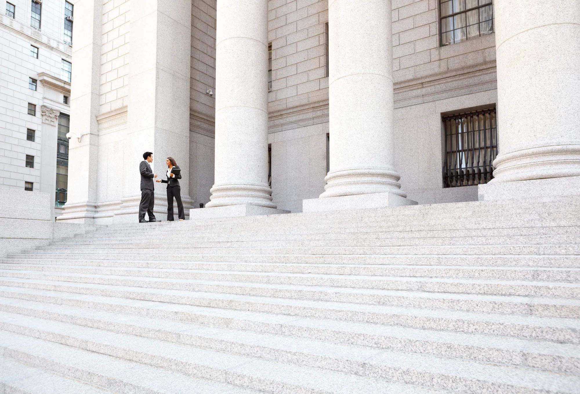 Two well dressed professionals in discussion on the exterior steps of a courthouse. Could be lawyers, business people etc.