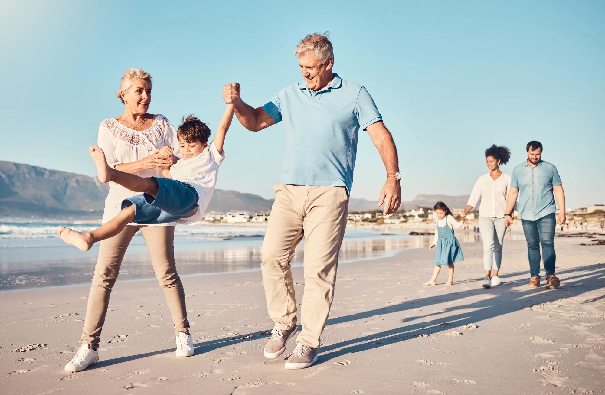 Swinging, grandparents and a child walking on the beach on a family vacation, holiday or adventure in summer. Young boy kid holding hands with a senior man and woman outdoor with fun energy or game.