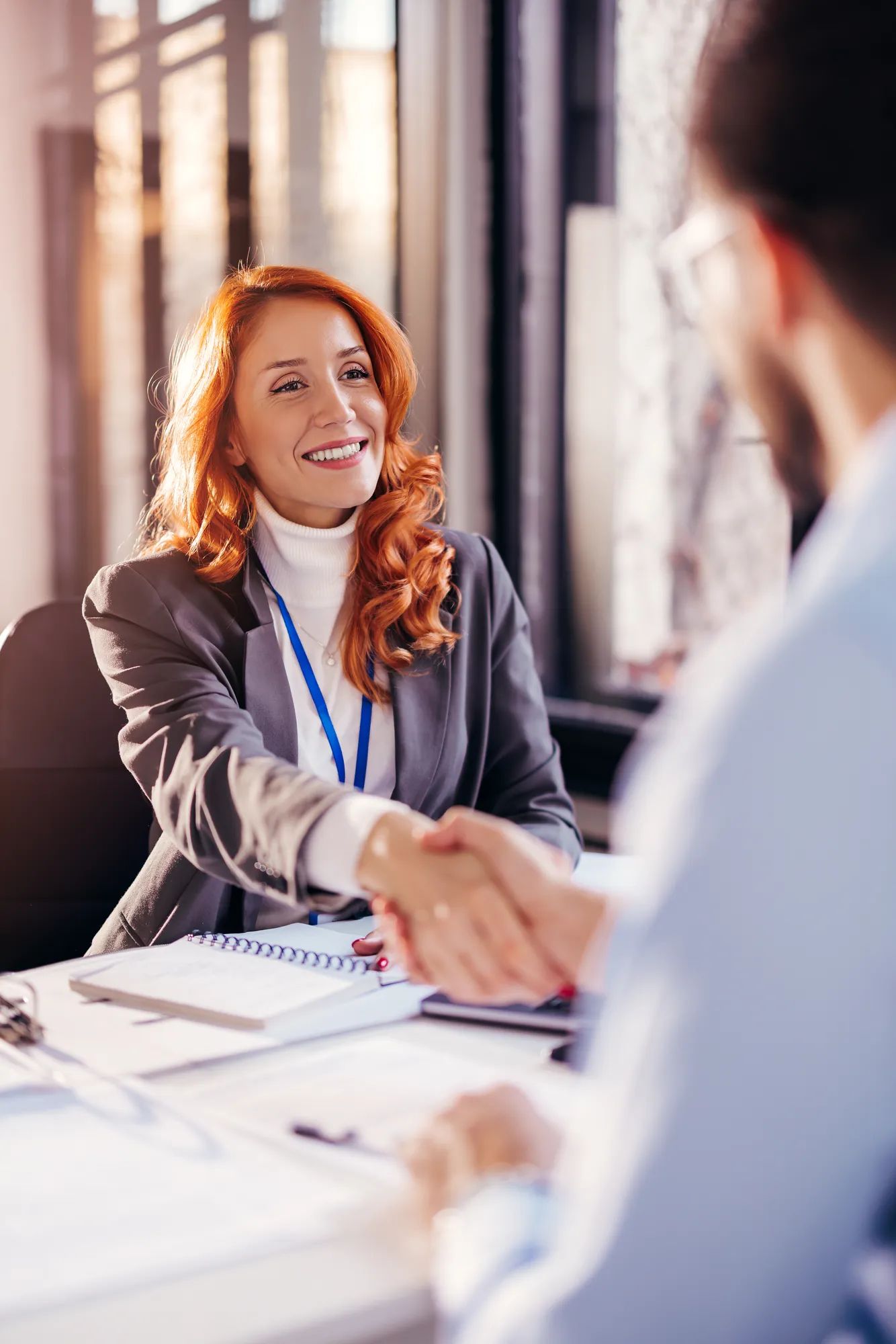  a young woman smiling and shaking hands with a client, after concluding a contract
