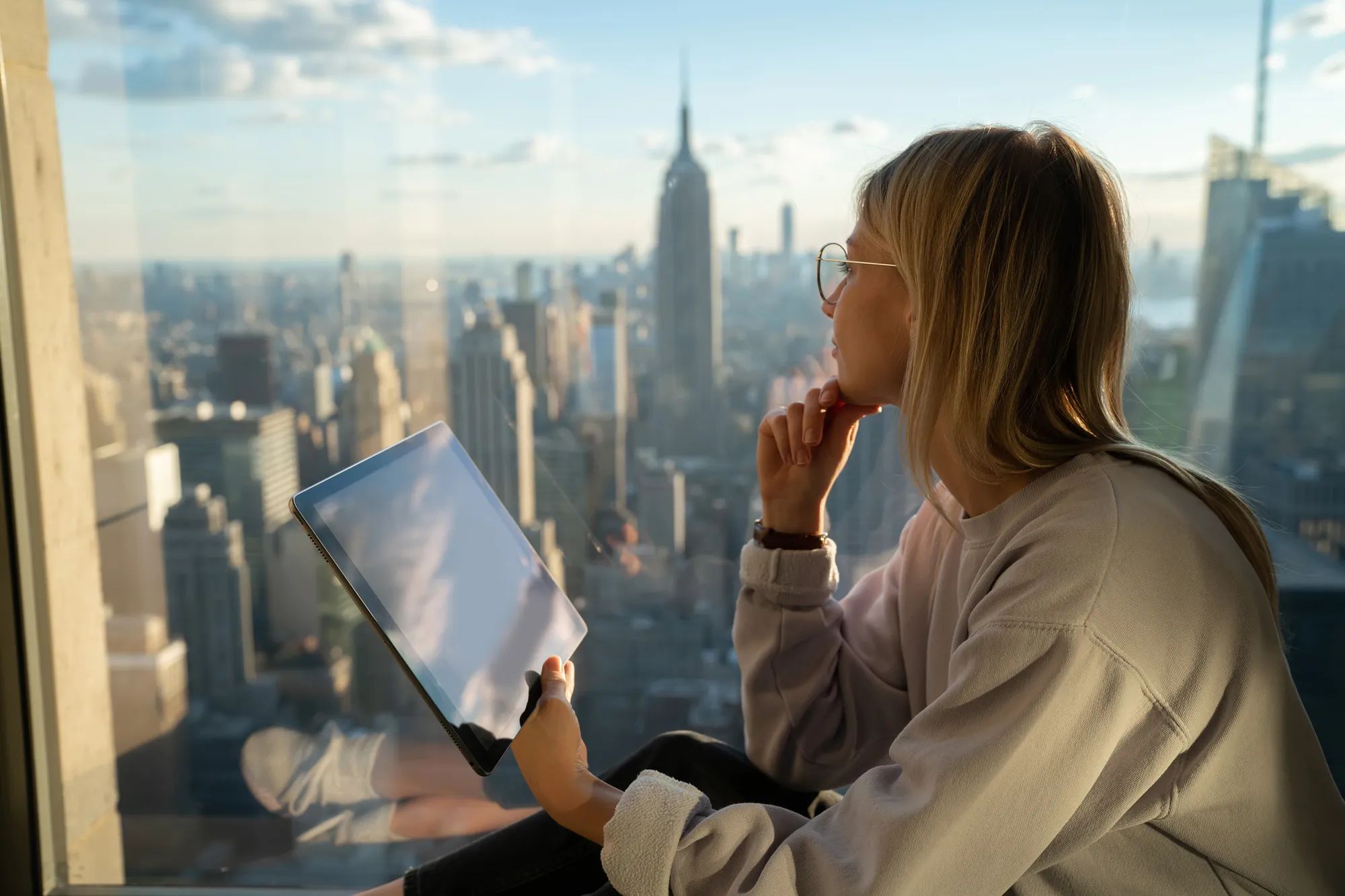 Thoughtful female with modern touch pad looking in panoramic window 