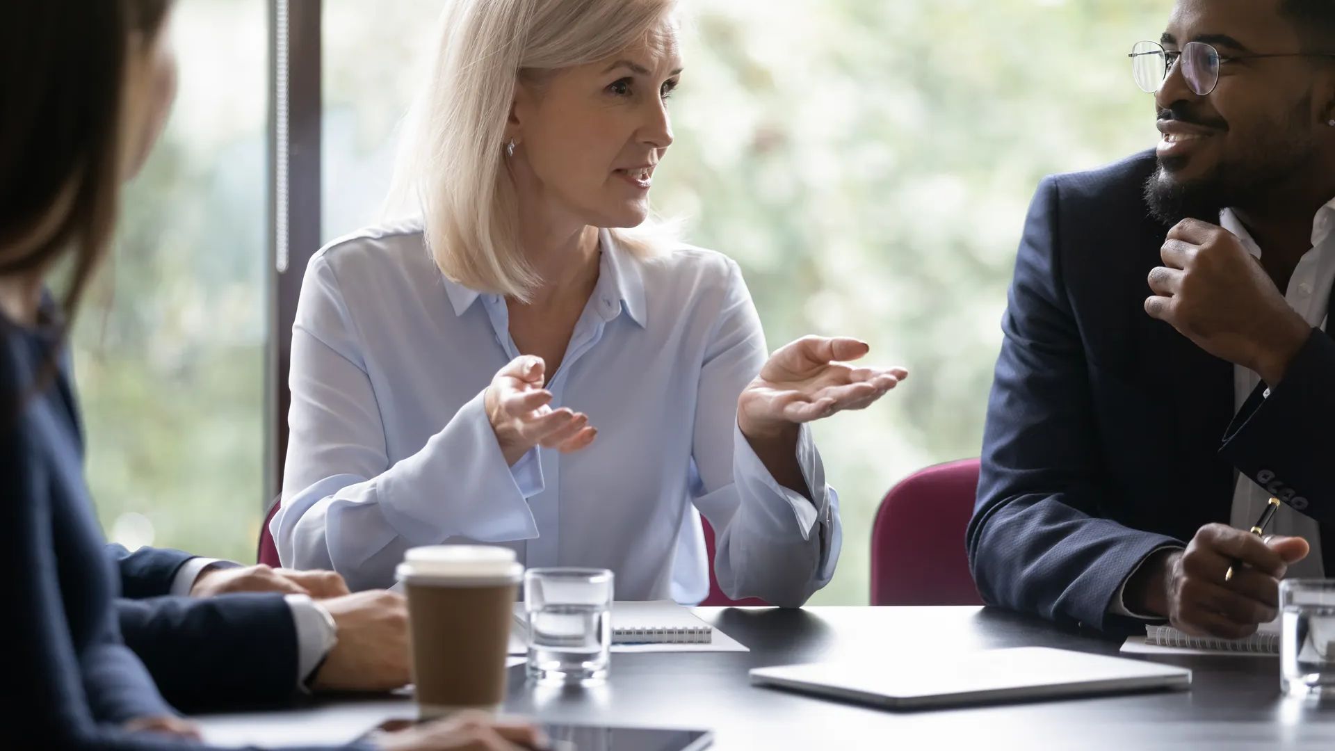 Friendly older woman business trainer or coach speaking to group of younger interns, senior female manager making proposition to clients on meeting, old lady executive talking on corporate briefing