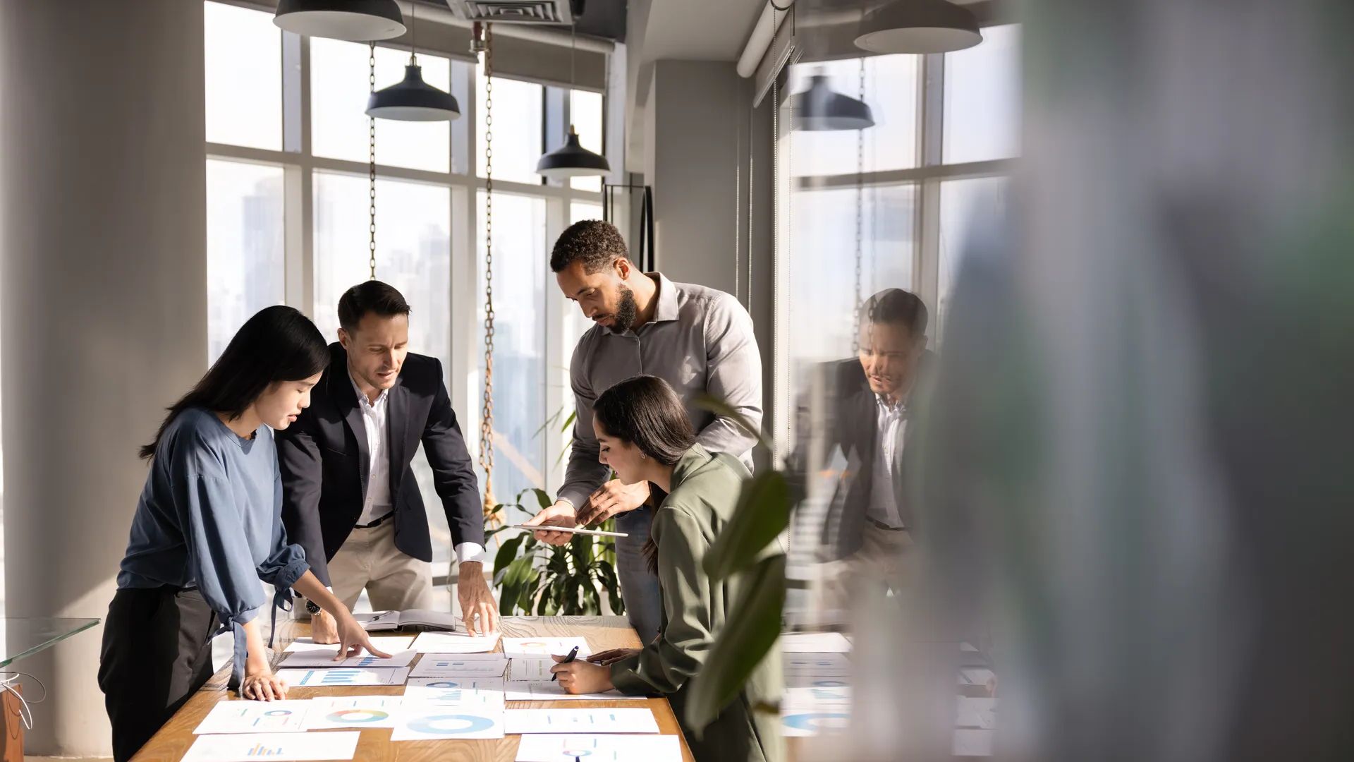 Four diverse business analysts discussing paper reports at meeting table, analyzing statistic research results, working together in business plan for project growth. Candid shot with copy space