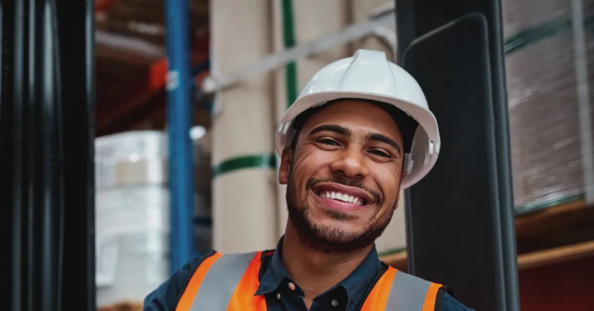 Happy forklift driver sitting in vehicle in warehouse