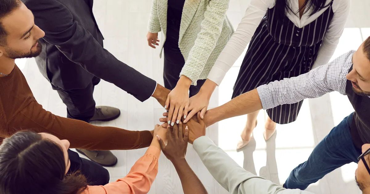 Happy diverse business team stacking hands. Mixed race group of young people standing in circle, putting hands together and smiling, high angle shot, top view, from above. Teamwork and support concept