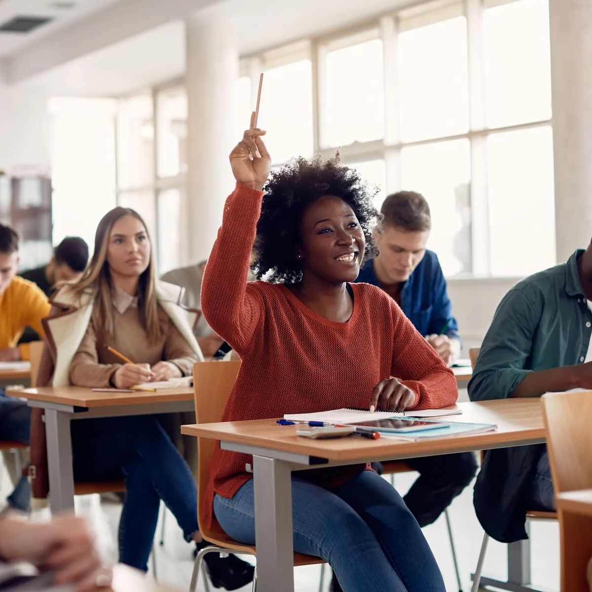 Happy African American student raising her hand to ask a question during lecture in the classroom. 