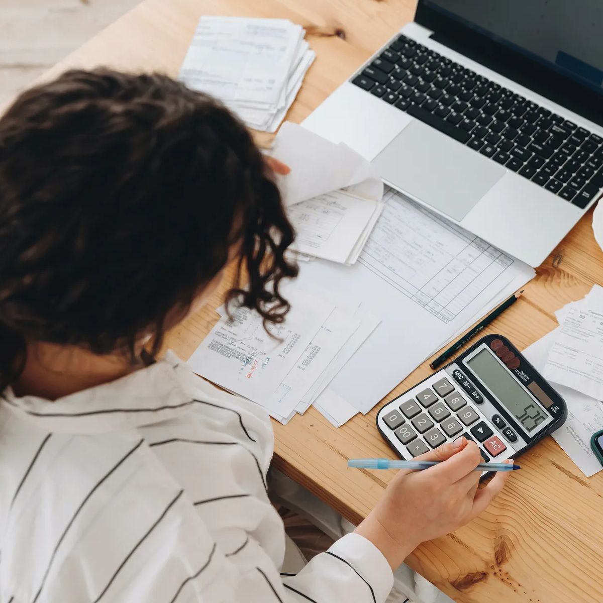 Top view of a woman working at home in the kitchen with financial papers, counting on a calculator, paying bills, planning a budget to save some money. Independent accounting, remote accountant.