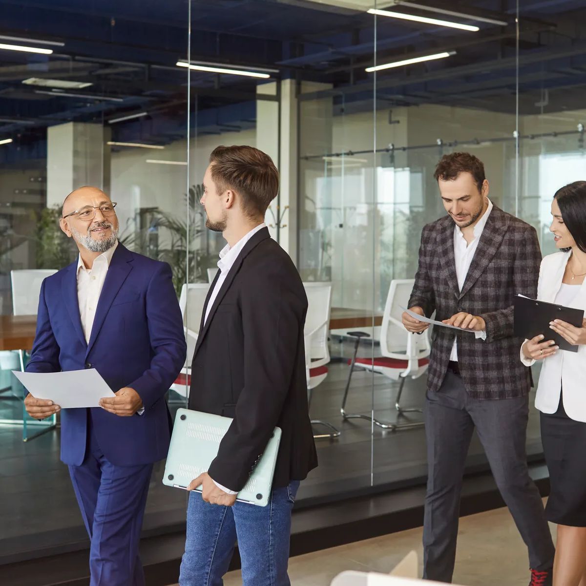 Business people team walking together in modern glass office corridor to discuss corporate meeting, financial data in paper documents. Group of busy professional employees brainstorming