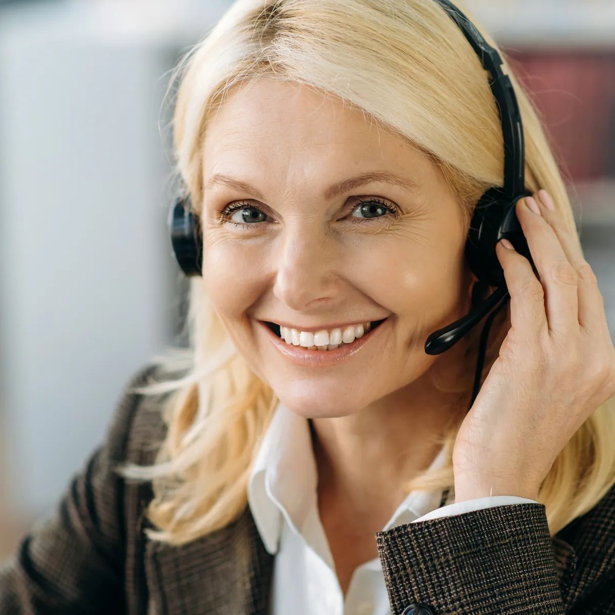 Close-up portrait of a middle aged charming blonde woman wearing headset.Caucasian friendly lady works as call center operator or at support line, consulting clients, looking at the camera and smiling