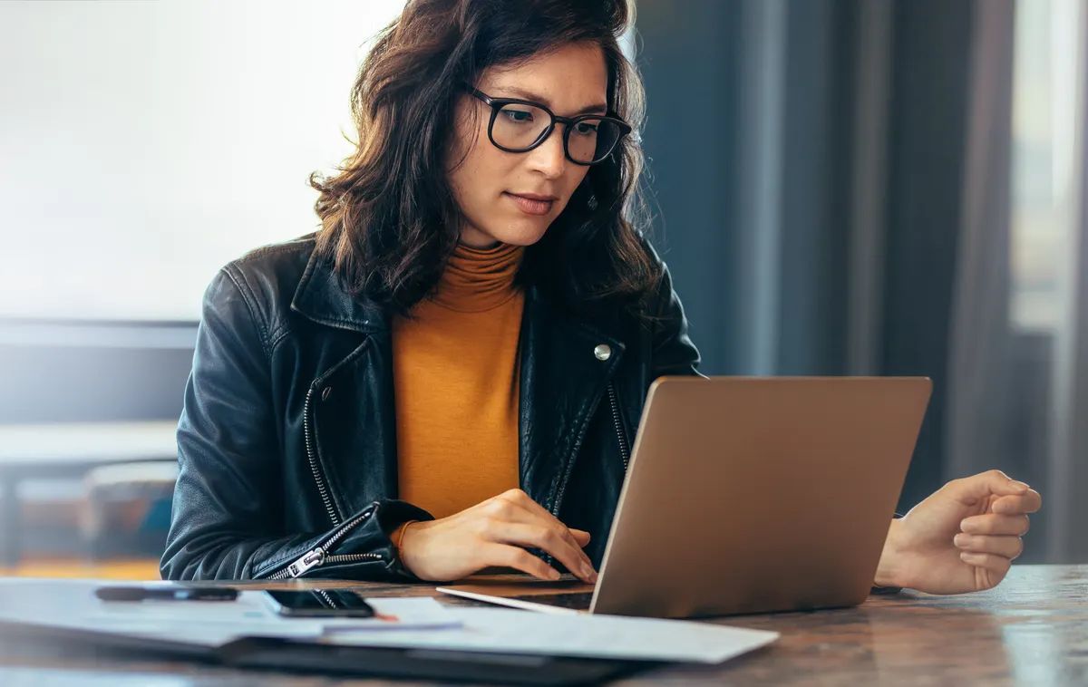 Asian business woman sitting at a table in an office, typing on her laptop with focus. Young female professional showing a dedication and commitment to her project at work.