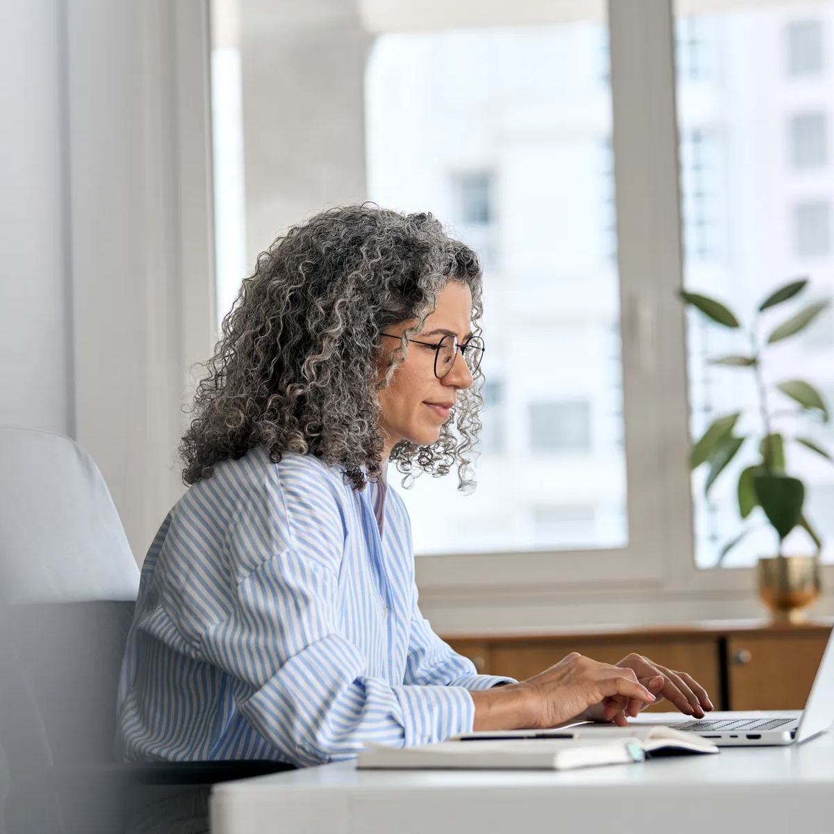 Busy mature senior business woman working in office using laptop. Middle aged old professional lady executive manager looking at computer digital technology sitting at desk. Authentic candid shot.