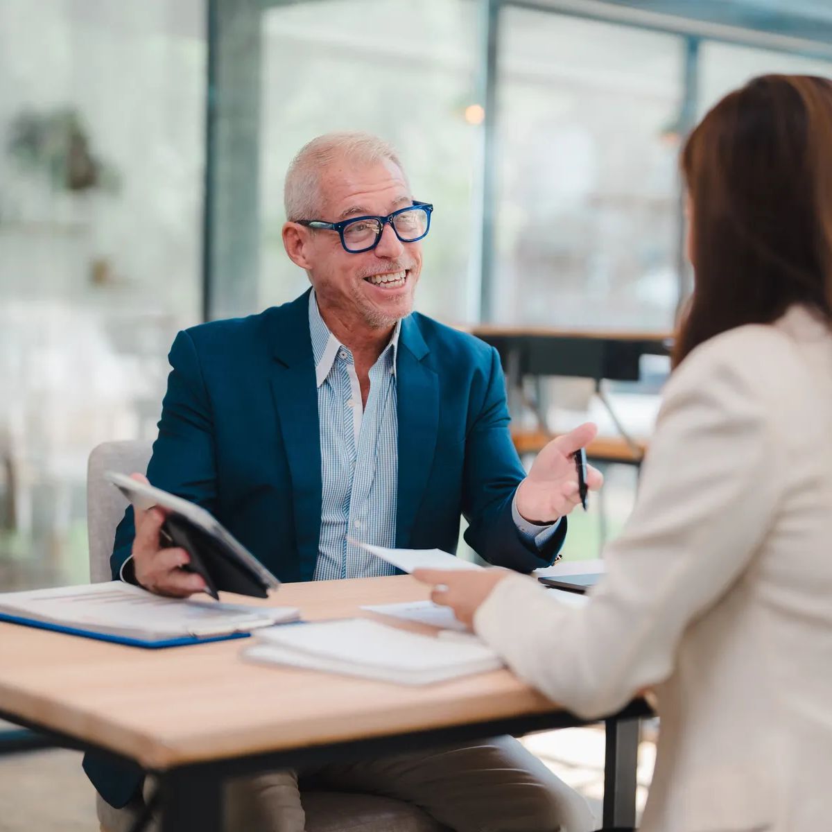 Senior manager explaining marketing strategy to his young female colleague during a business meeting in a modern office, they're analyzing financial reports using a tablet and paper documents