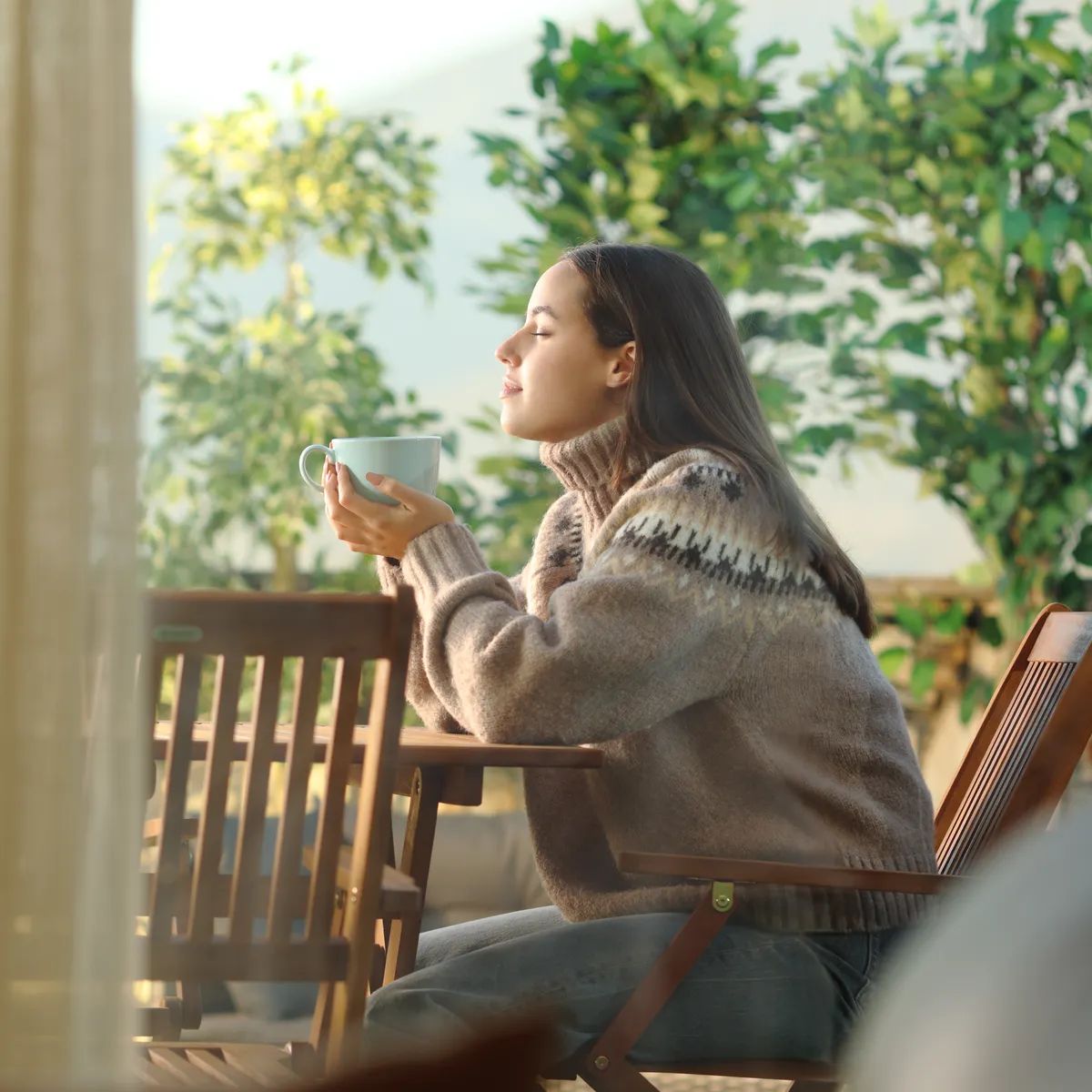 Side view portrait of a woman sitting in a terrace relaxing and drinking coffee at home