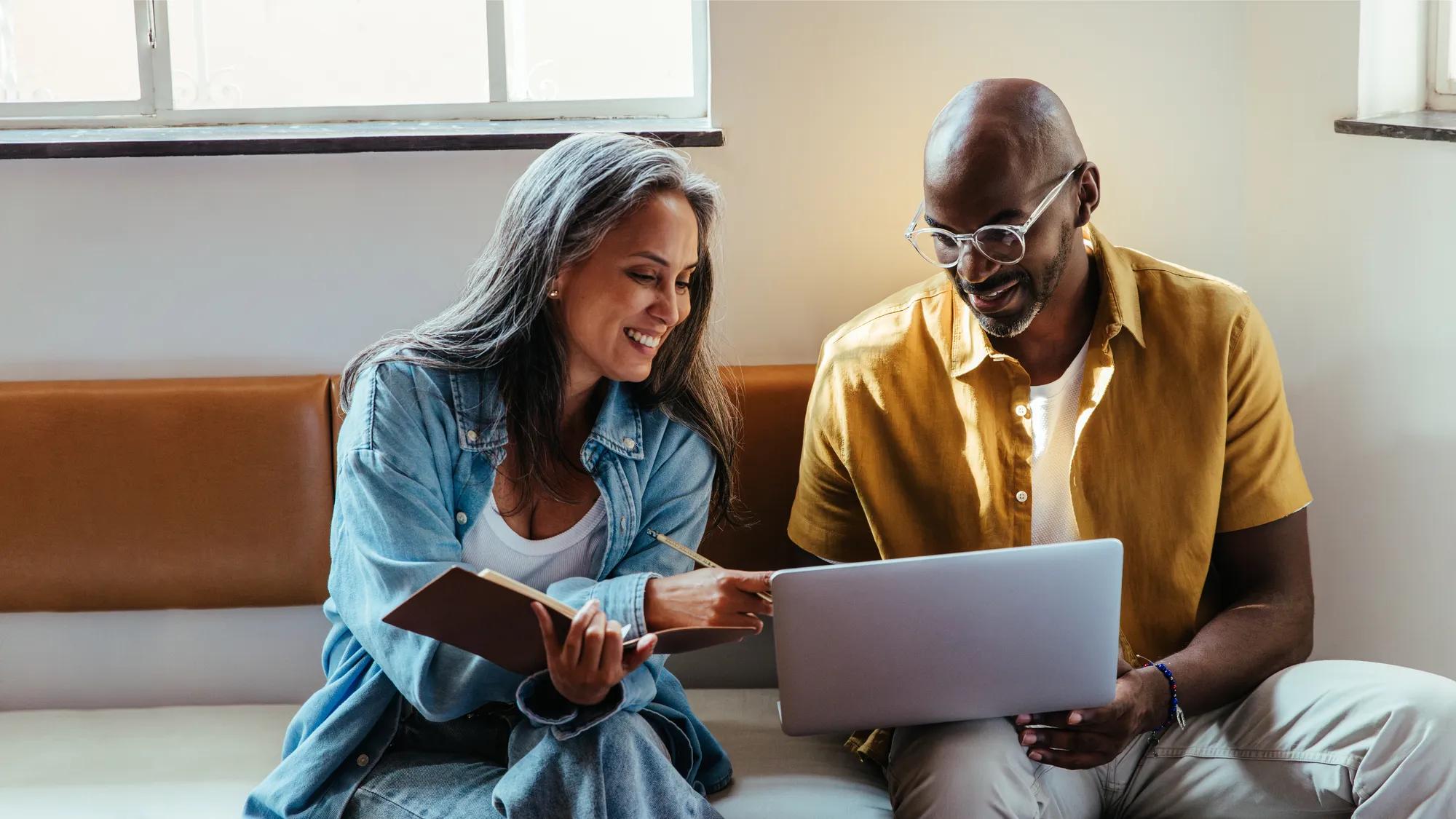 Team collaboration between a mature black man and woman sitting and discussing work with a laptop in a modern setting.