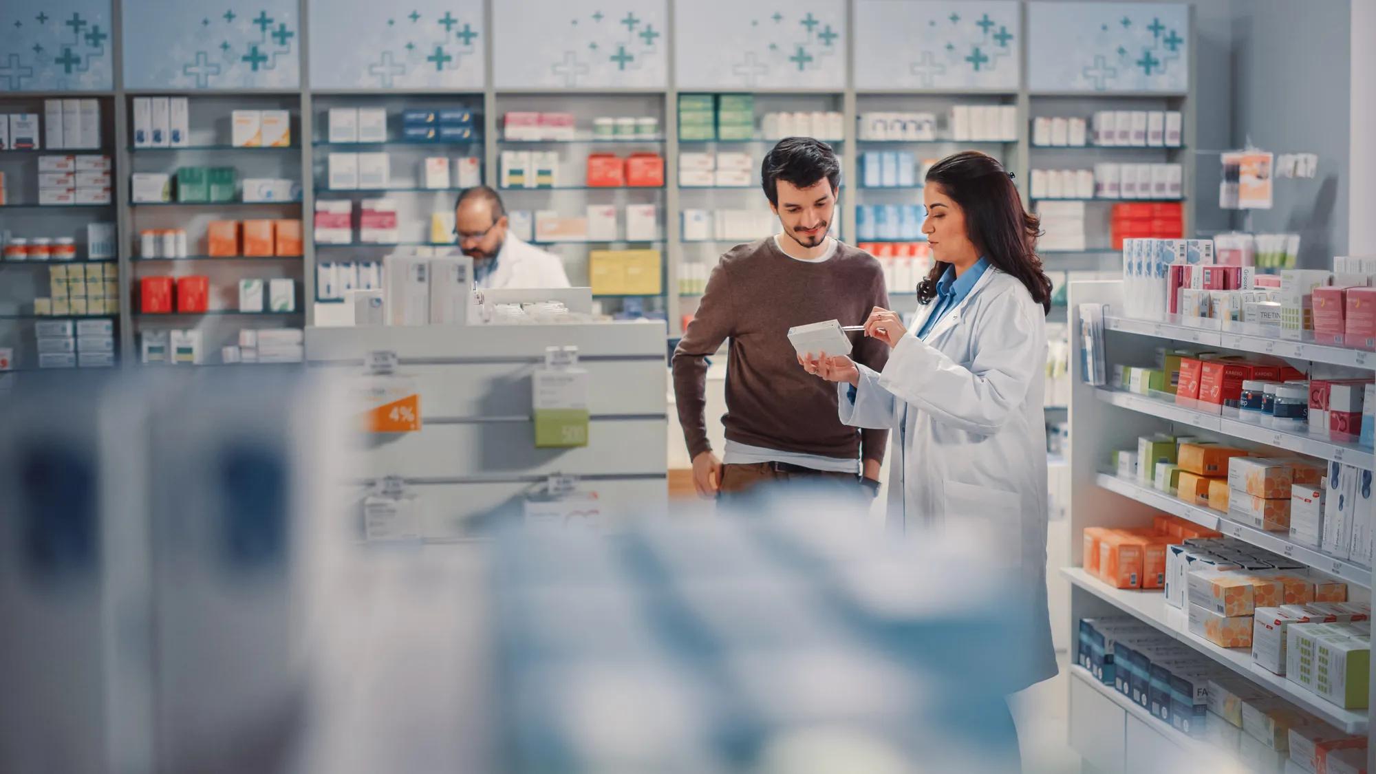 Pharmacy Drugstore: Handsome Hispanic Man Chooses to Buy Medicine, Drugs, Vitamins, Professional Pharmacist Helping Customer with Recommendation. Modern Pharma Store Shelves with Health Care Products.