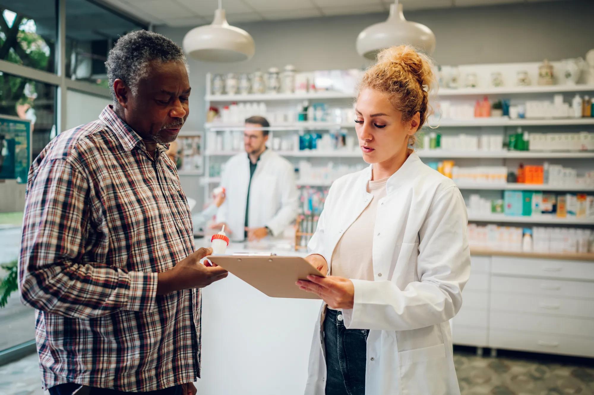 A pharmacist in a white coat engaged in a warm, consultative conversation with a client at a pharmacy counter. Both individuals are attentive and engaged, suggesting a supportive, professional interaction around medication or treatment options. The setting is a modern, well-lit pharmacy environment. The tone is approachable and trustworthy, reflective of personalized healthcare guidance.