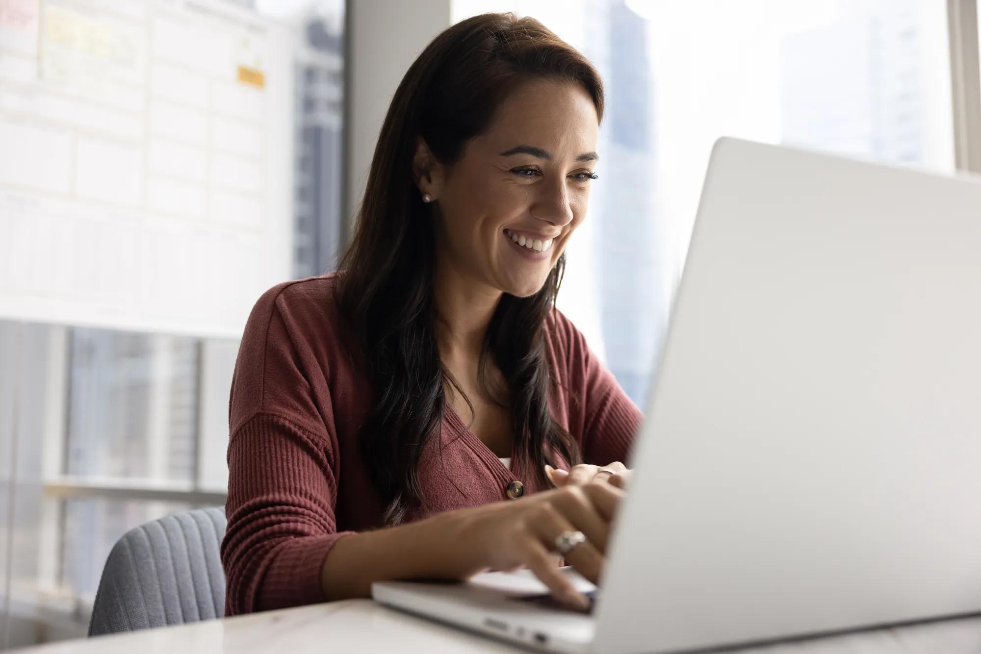 Enjoying work success. Cheerful happy young businesswoman typing on notebook at office desk smiling starting workday with enthusiasm bring joy motivation to daily routine inspired by good job result