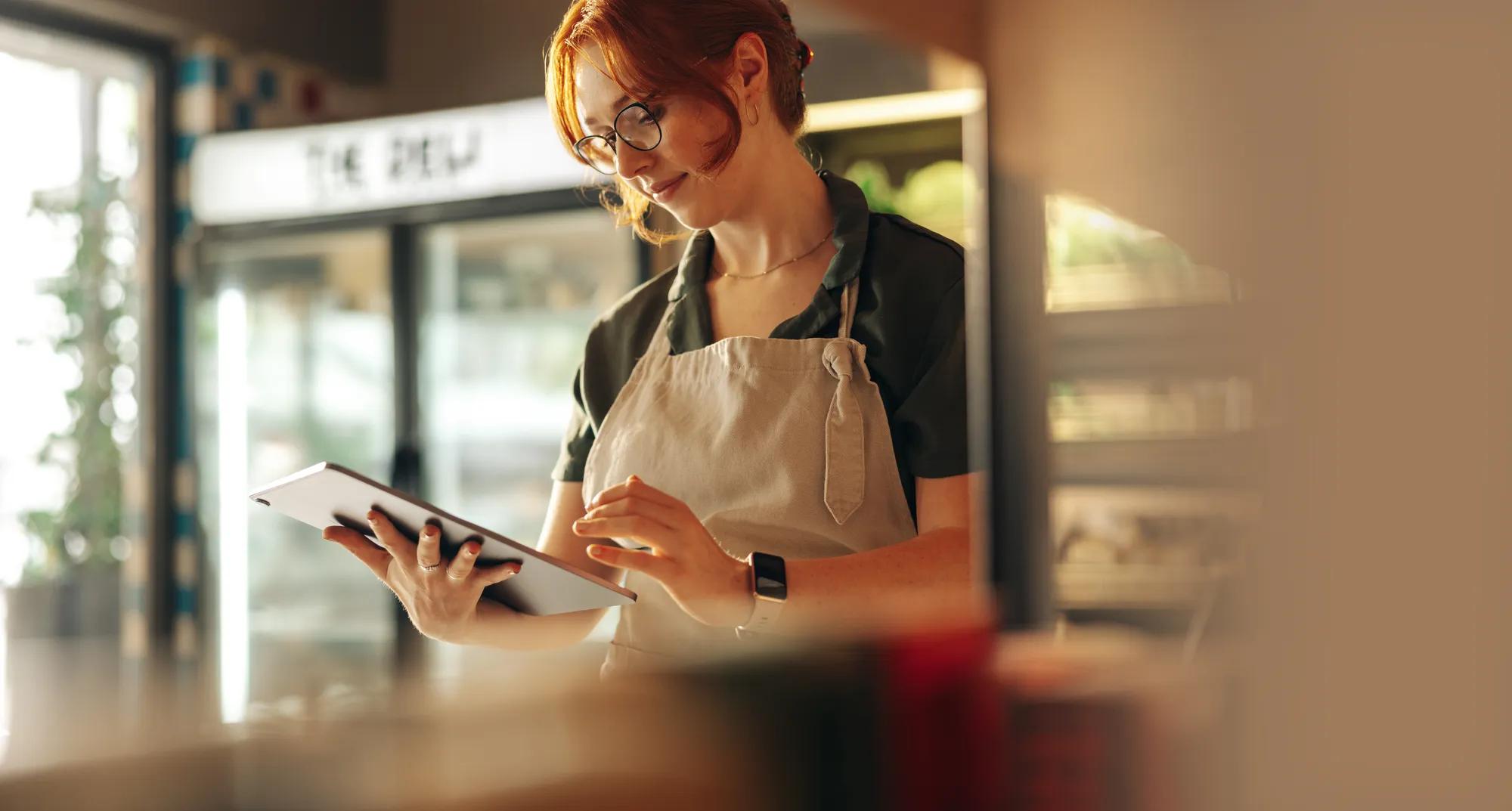Cheerful shop owner using a digital tablet while standing in her grocery store. Successful female entrepreneur running her small business using wireless technology.