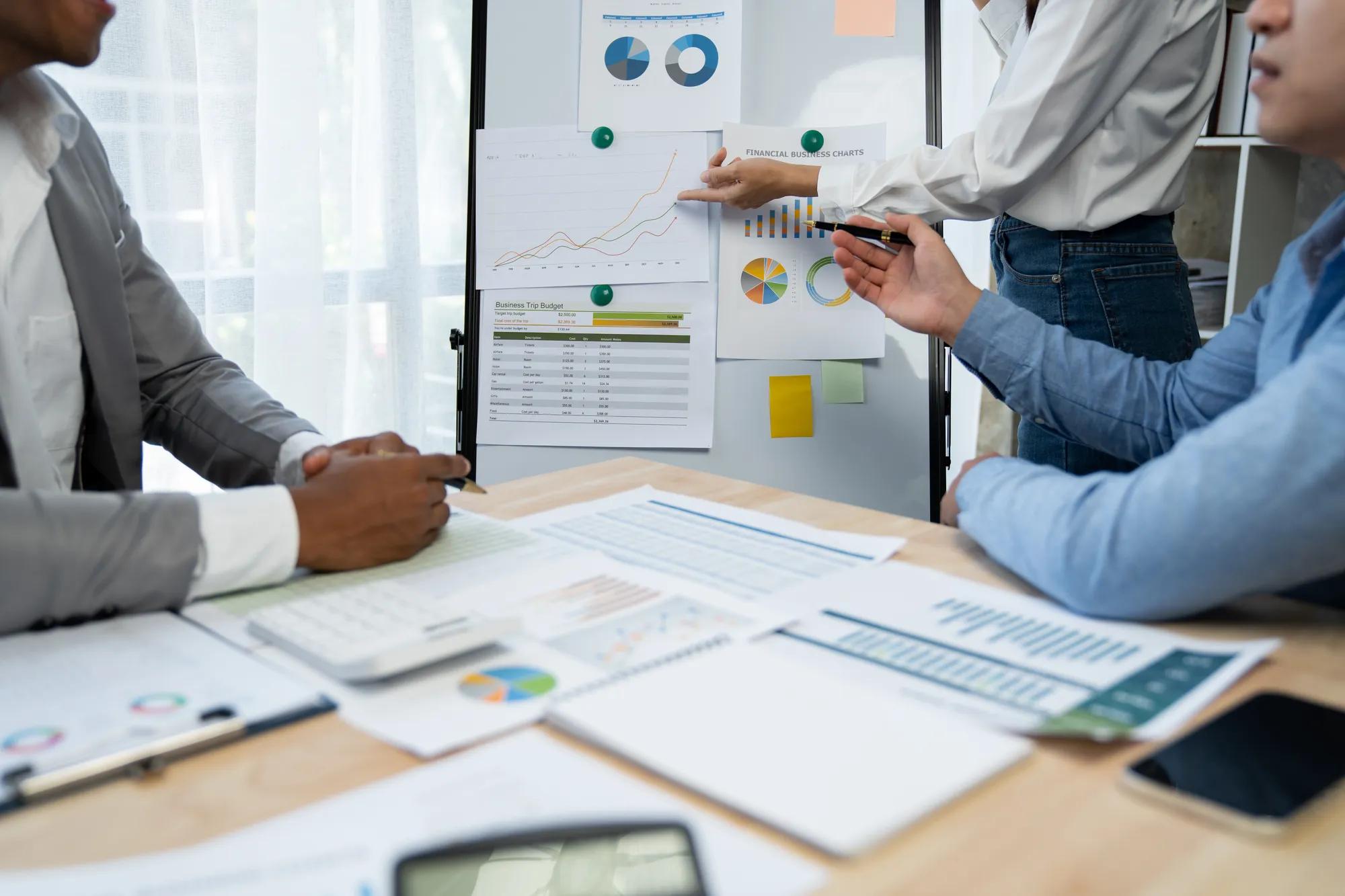 Group of Asian businessmen, and financial analysts pointing to data graphs and financial comparison documents to audit accounts. and administrative results conference management concept.